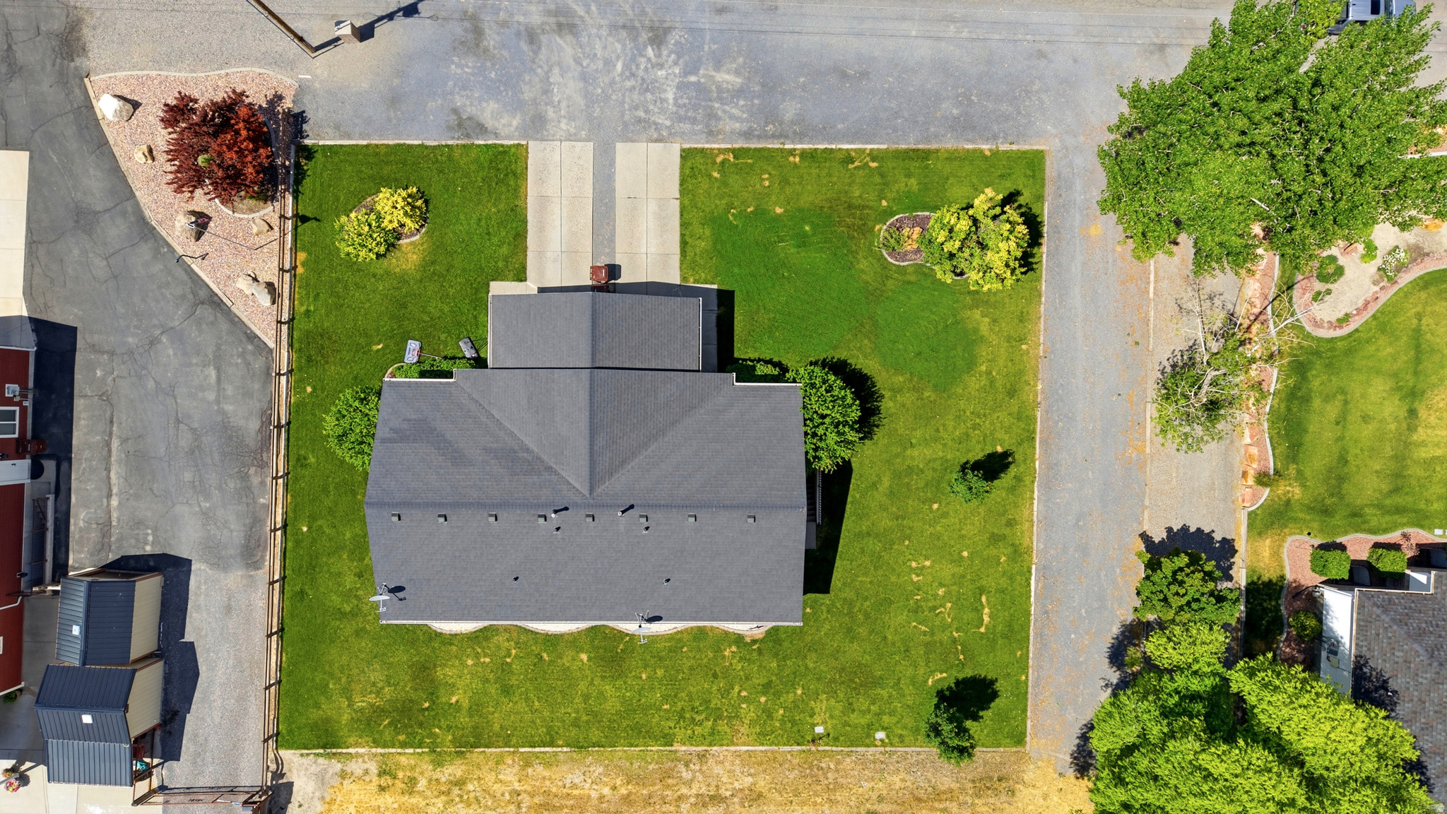 Aerial perspective showcasing a property with a dark shingle roof, green lawn, and concrete driveway