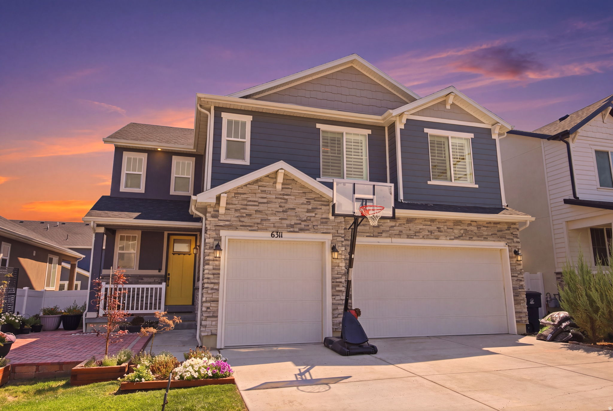 Two-story residence featuring a stone and siding facade, a two-car garage, and a welcoming yellow front door