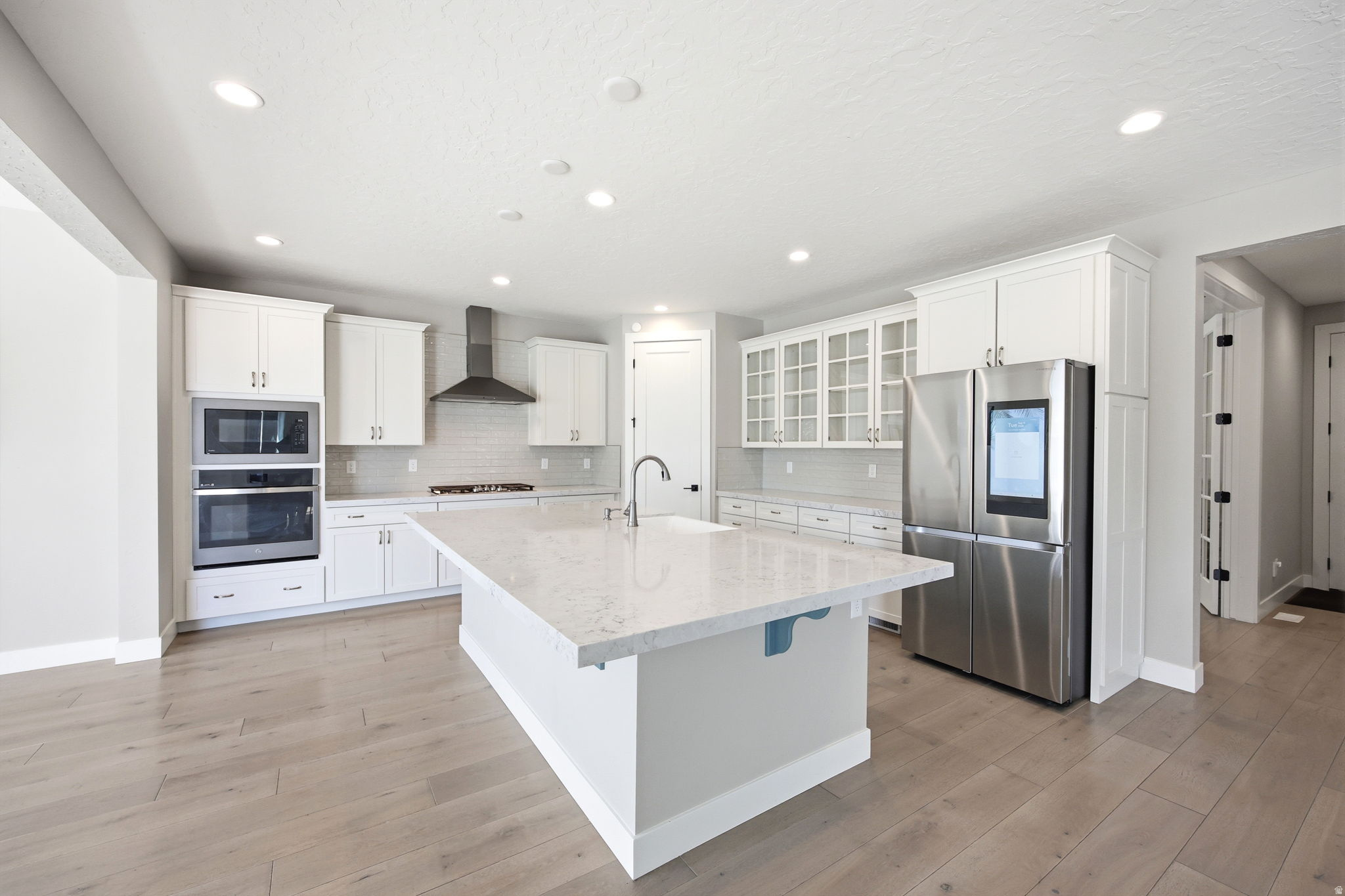 Gourmet kitchen featuring a large central island with a sink, white cabinetry, integrated stainless steel appliances, a tile backsplash, and light wood-finish flooring