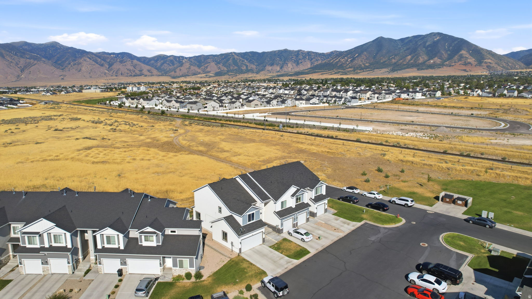 Expansive aerial view showcasing this residence situated on a generous lot with manicured landscaping, paved driveway, and detached garage