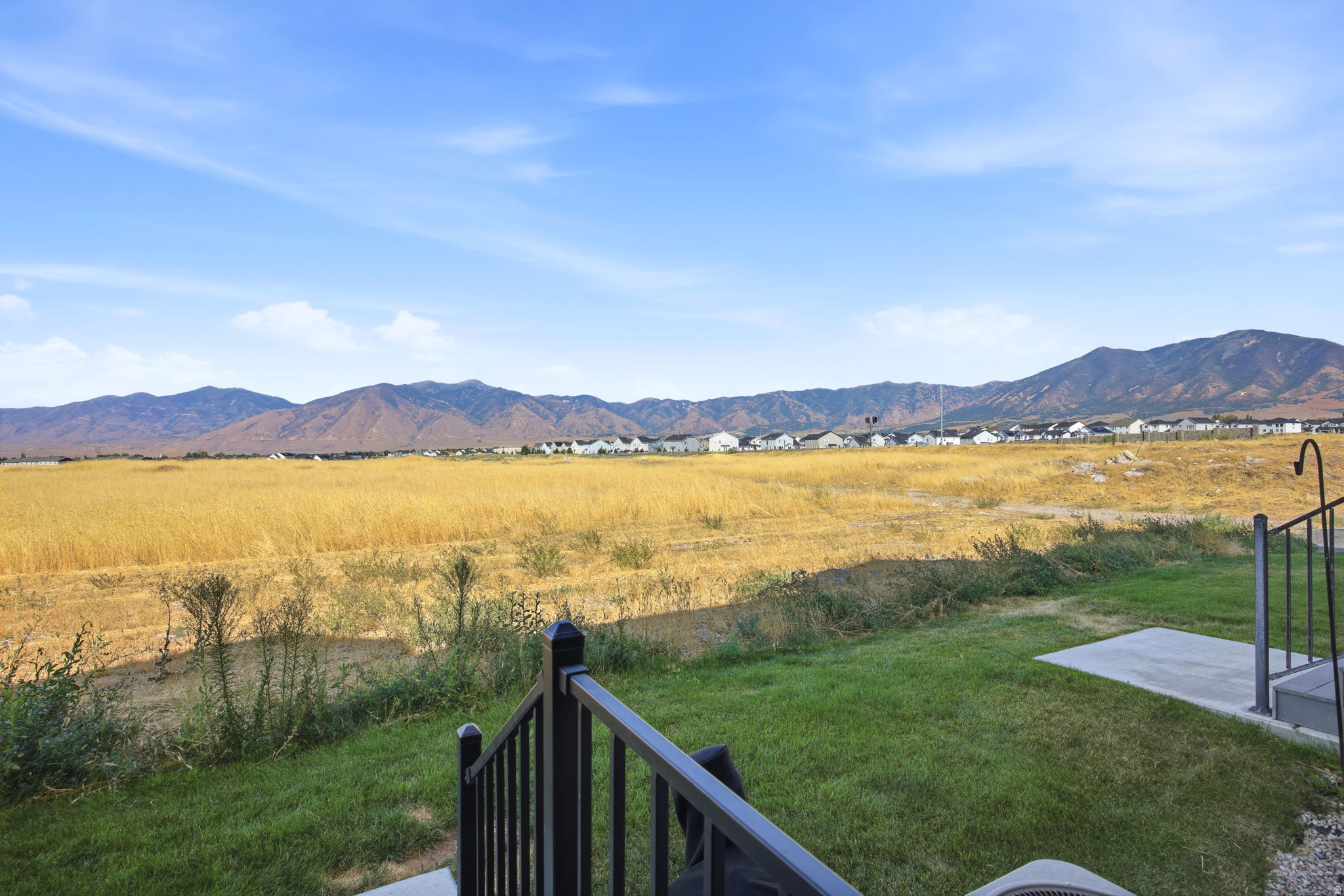 Expansive backyard with mature lawn and black metal railing, overlooking rolling grassland and distant mountain range