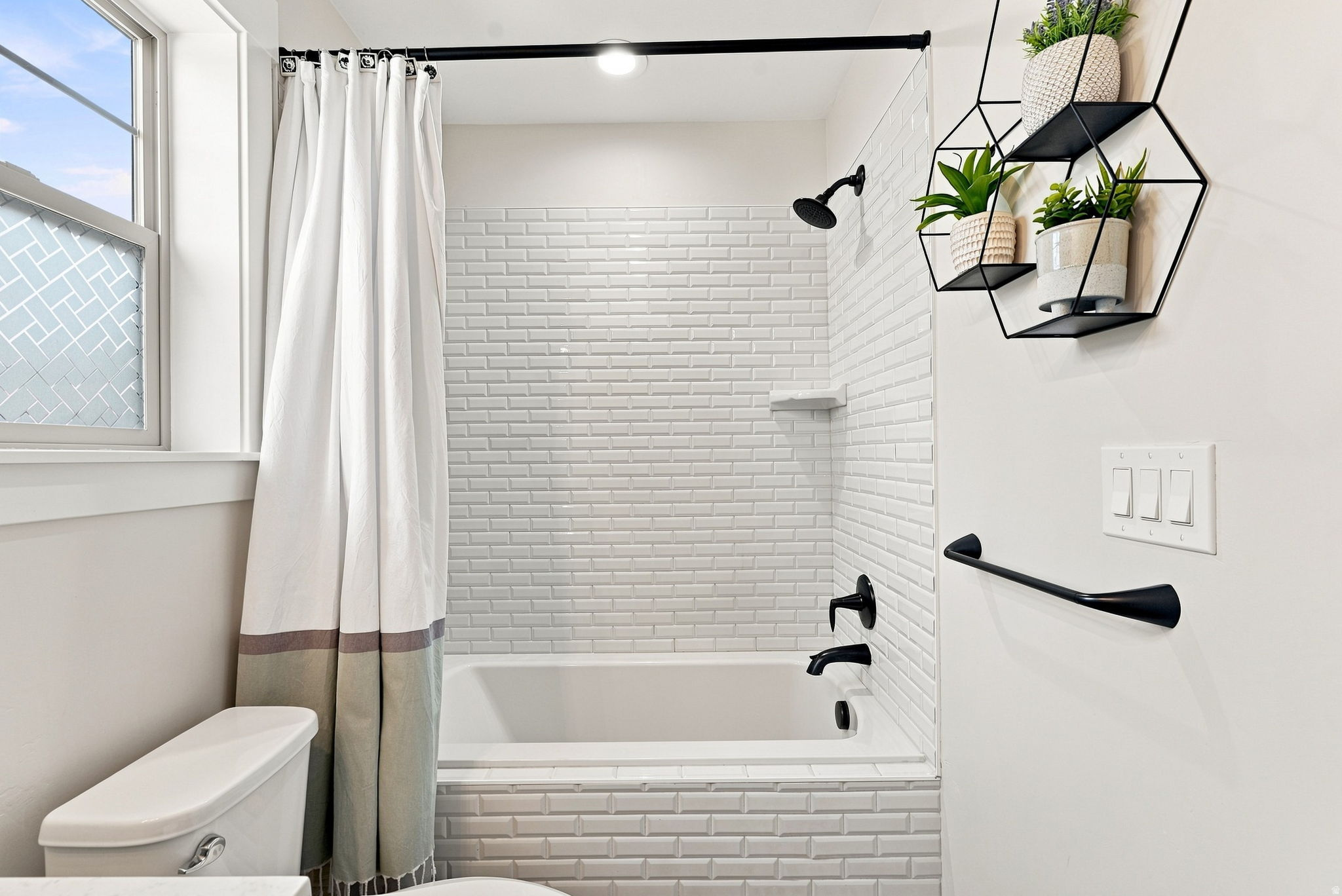 Bathtub with white subway tile surround, matte black shower fixtures, and a clear glass shower screen