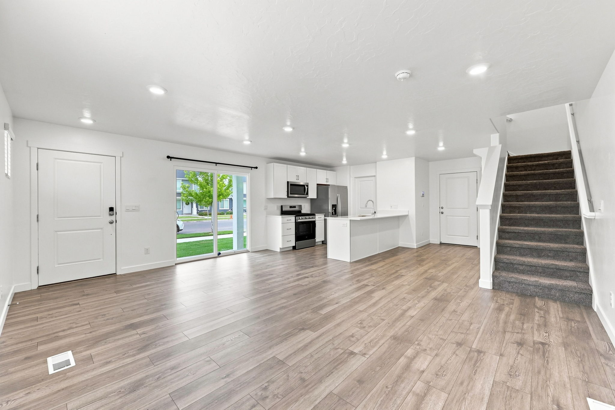 Open-concept living area featuring wood-finish flooring, recessed lighting, a kitchen with white cabinetry, stainless steel appliances, and a breakfast bar