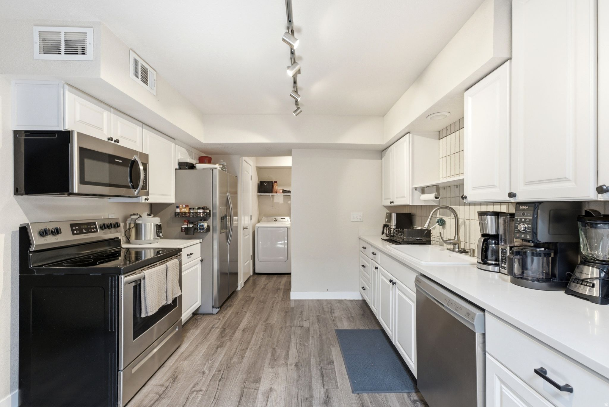 Kitchen featuring white cabinetry, stainless steel appliances, wood-finish flooring, and a tile backsplash