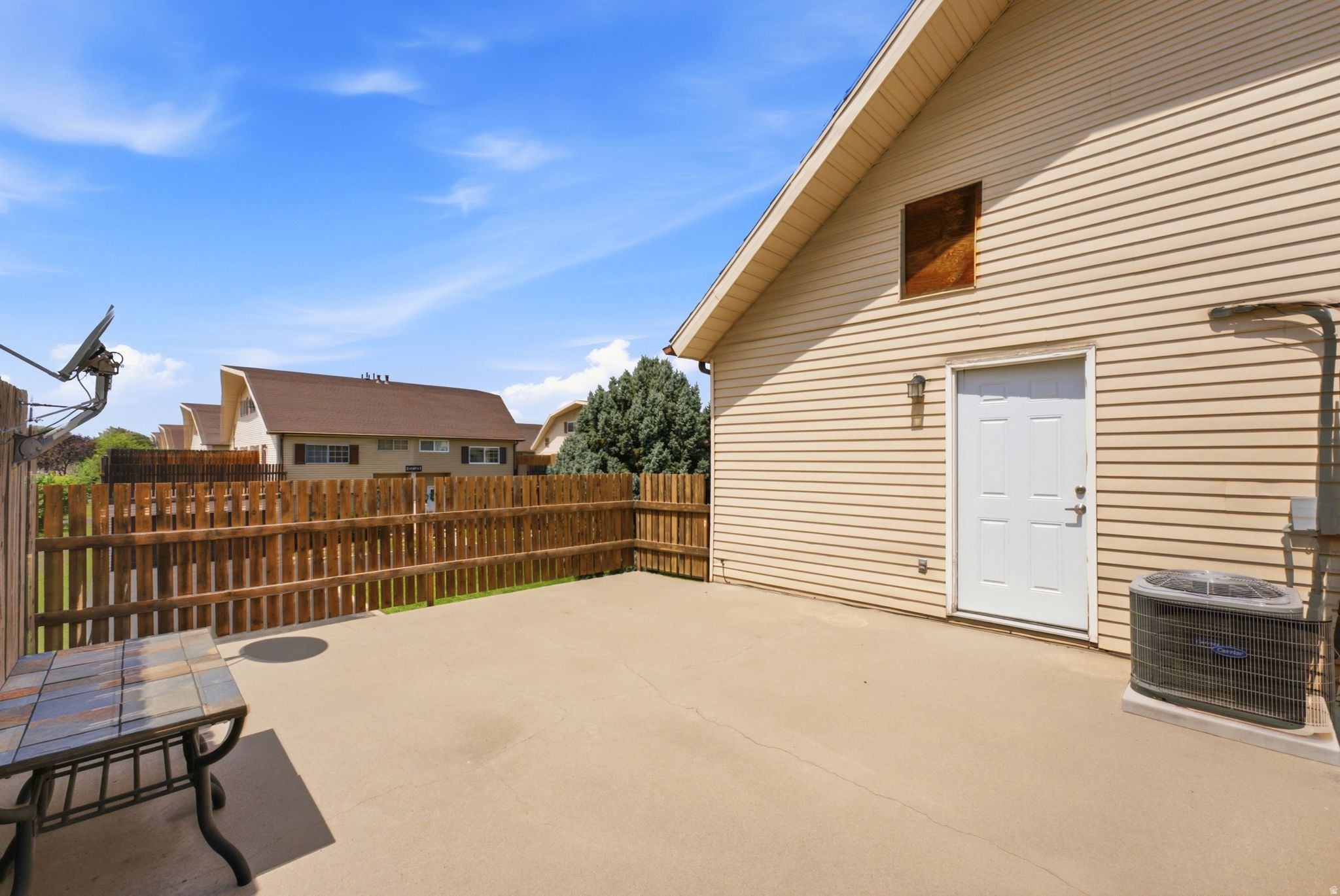Expansive concrete patio with wooden privacy fencing, mature landscaping, and direct access to the home's exterior