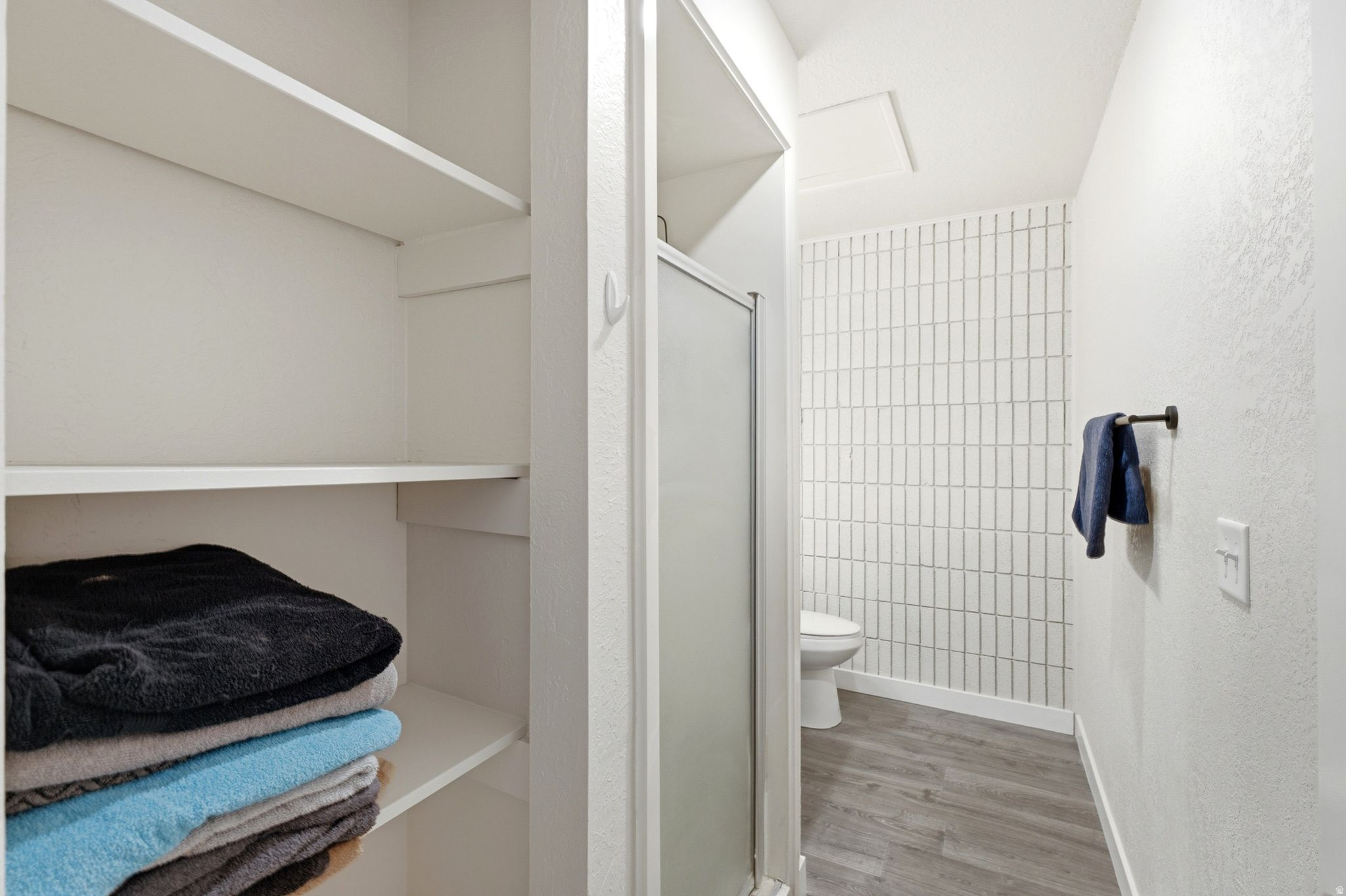 Efficient bathroom layout featuring white subway tile walls, wood-finish flooring, and a toilet with chrome fixtures