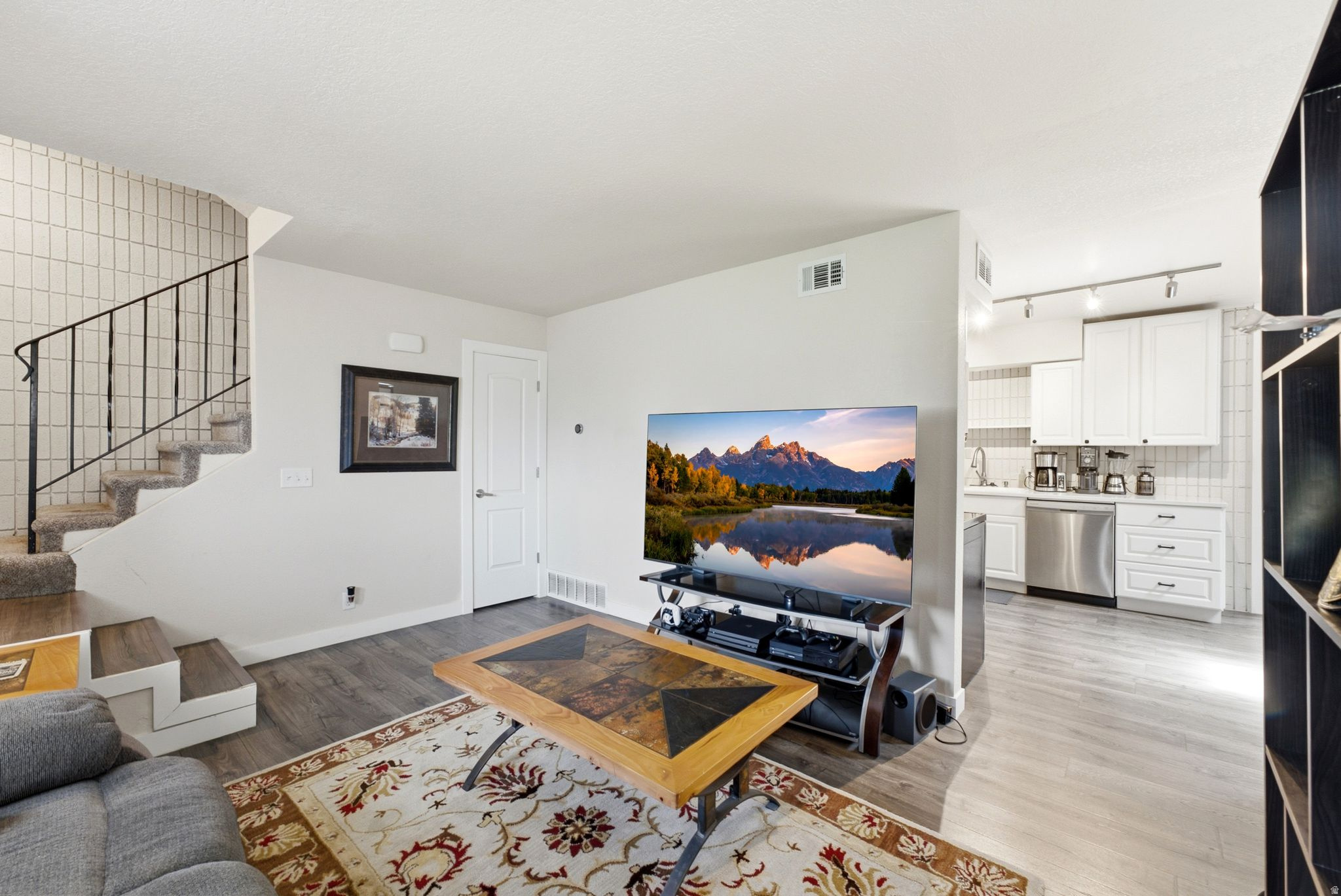 Open-concept living space featuring hardwood flooring, a gas fireplace with built-in entertainment cabinetry, and a well-appointed kitchen with white cabinetry and stainless steel appliances