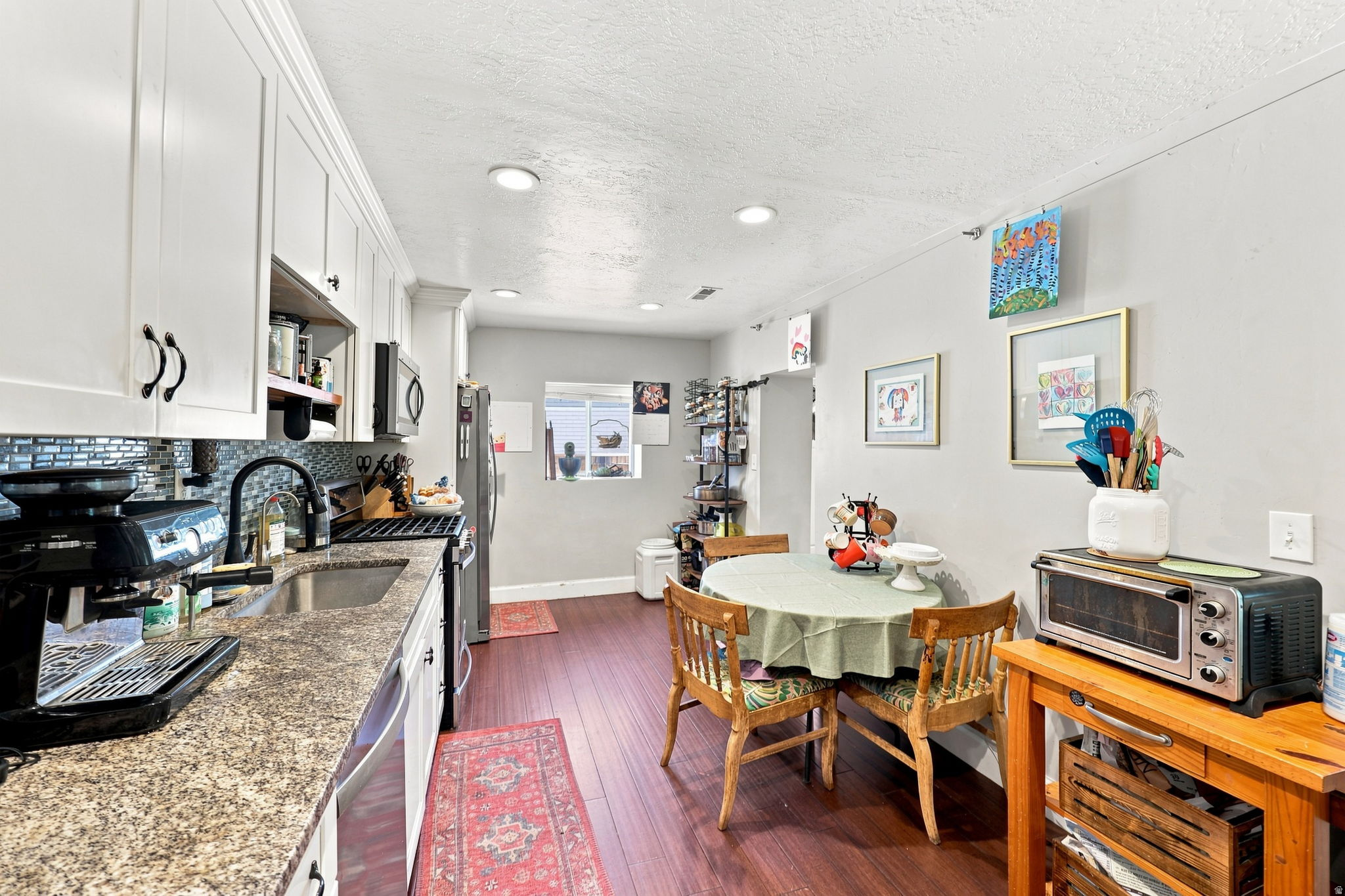 Kitchen featuring white cabinetry, granite-style countertops, stainless steel appliances, and wood-finish flooring
