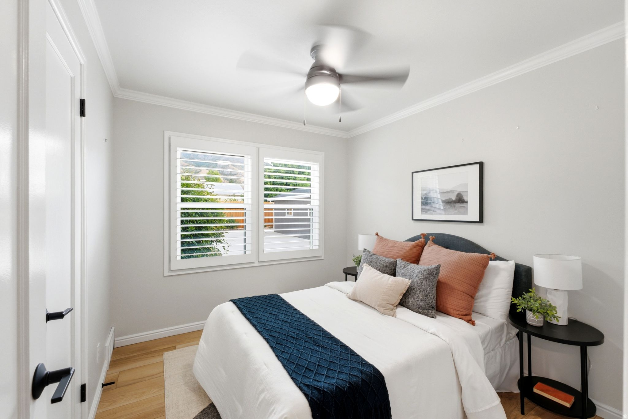 Bright bedroom featuring hardwood flooring, a ceiling fan with integrated lighting, and plantation shutters framing dual windows
