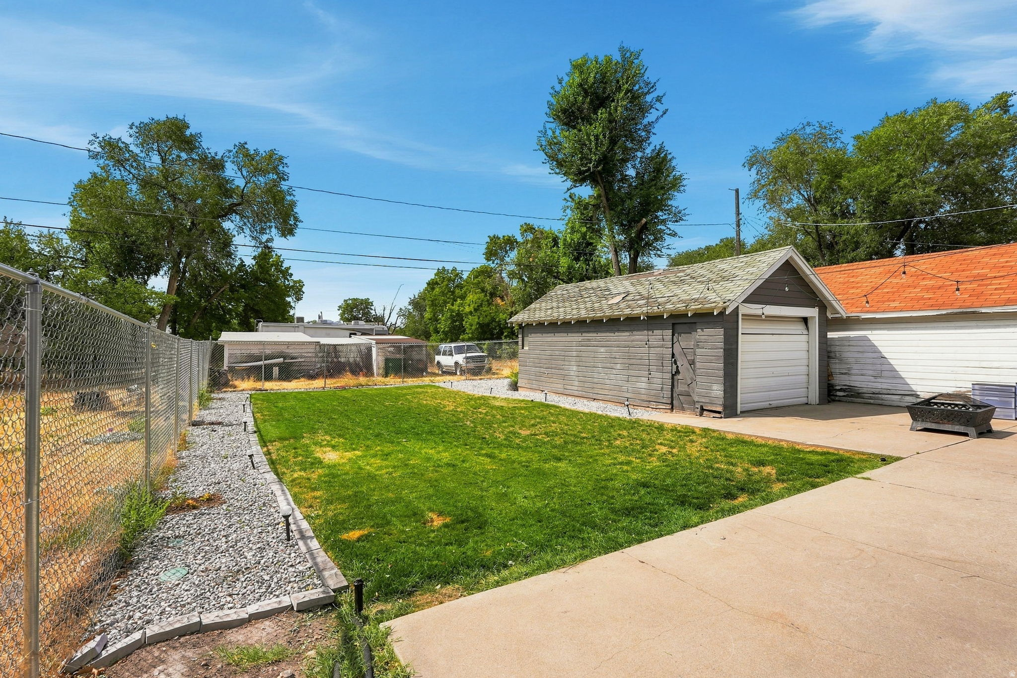 Expansive green space featuring a concrete patio, detached garage, chain-link fencing, and gravel landscaping