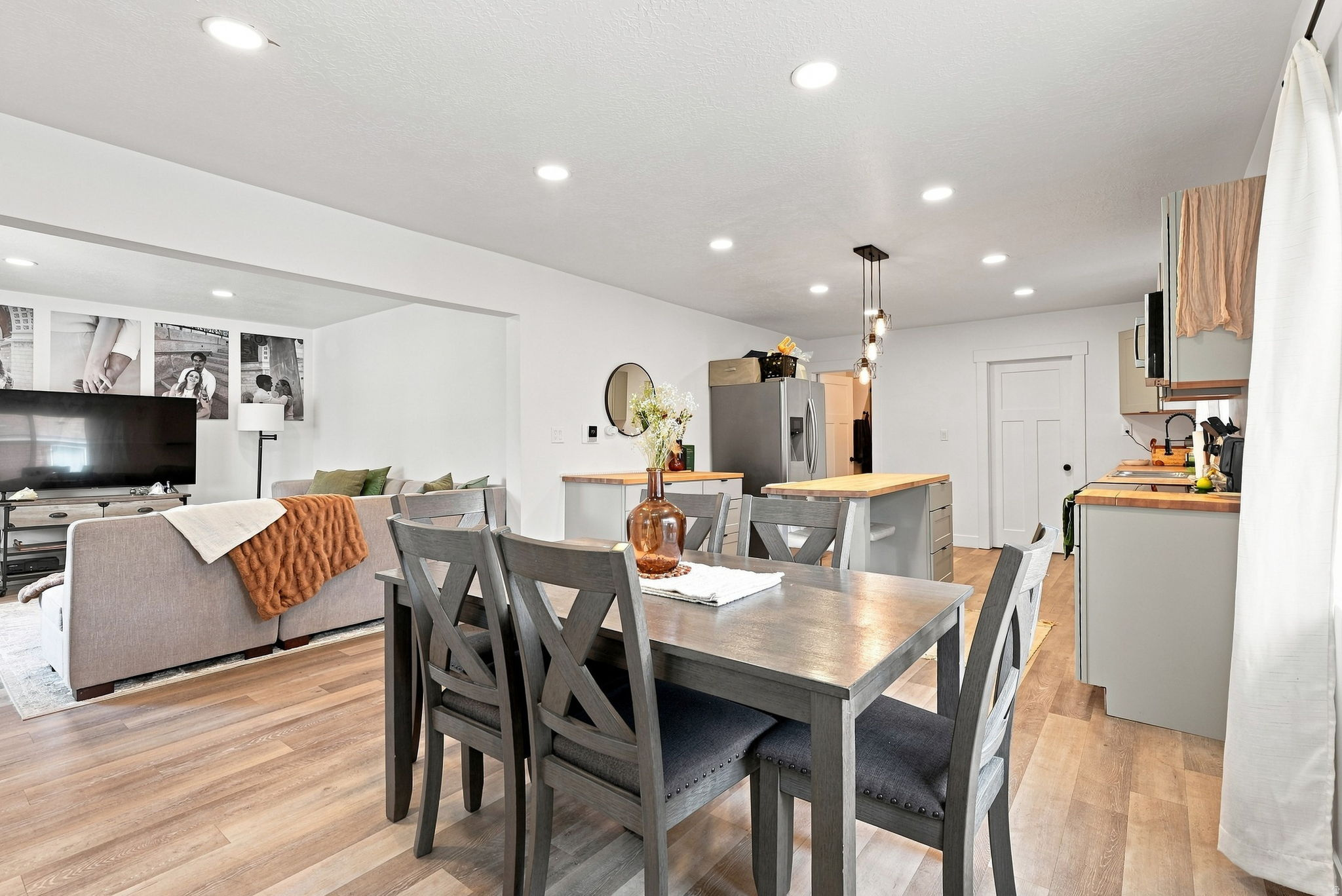 Open-concept living area featuring a wood-finish dining table with seating for four, pendant lighting above, and seamless integration with the kitchen