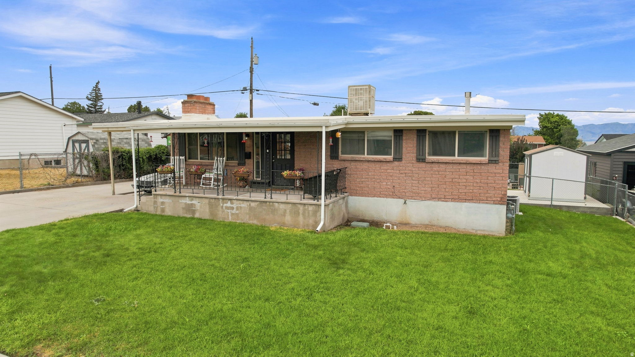 Brick exterior, covered front porch, carport, mature landscaping, and an external storage shed