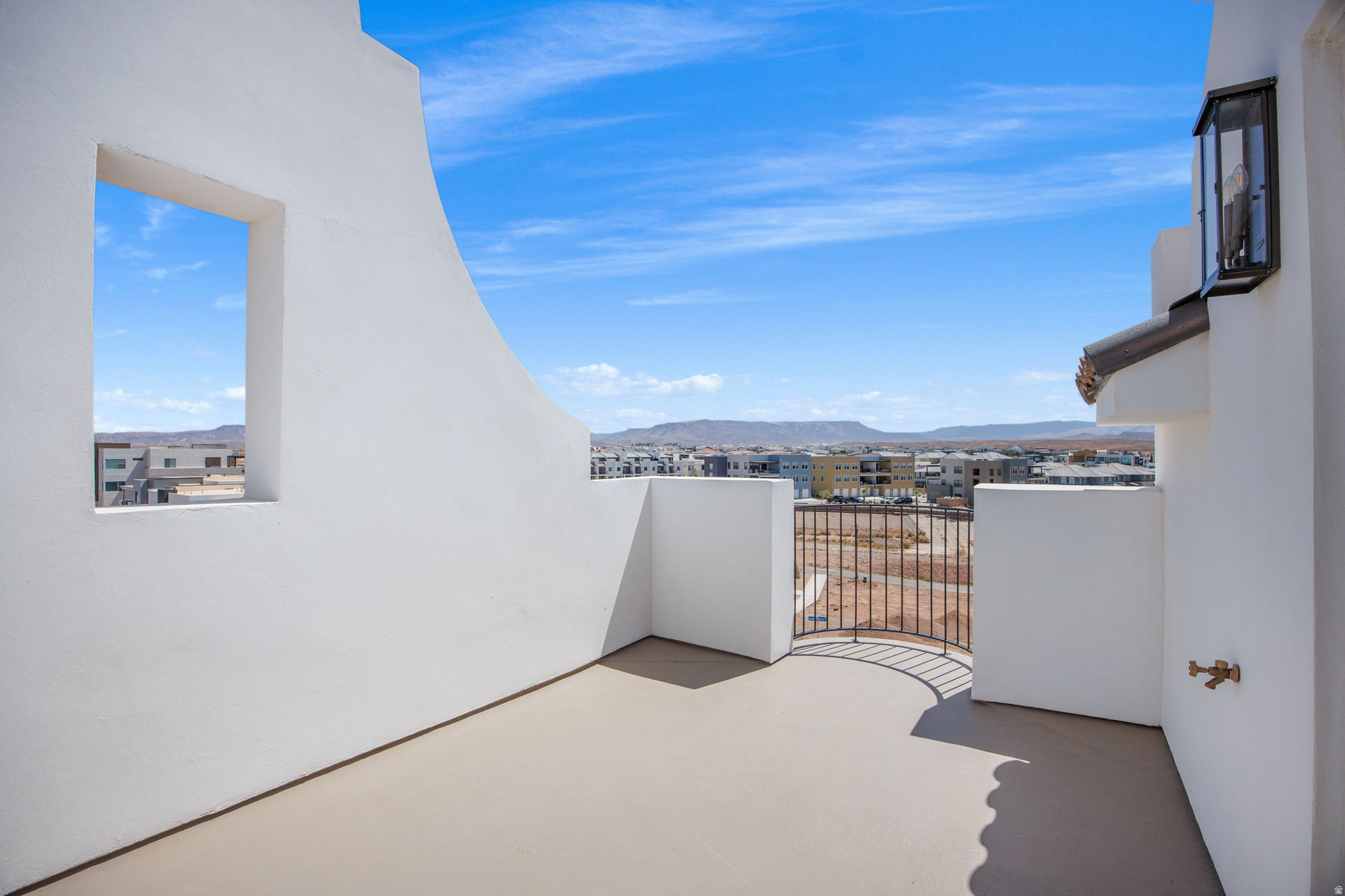 Rooftop patio with white stucco walls, decorative iron railing, and distant mountain scenery