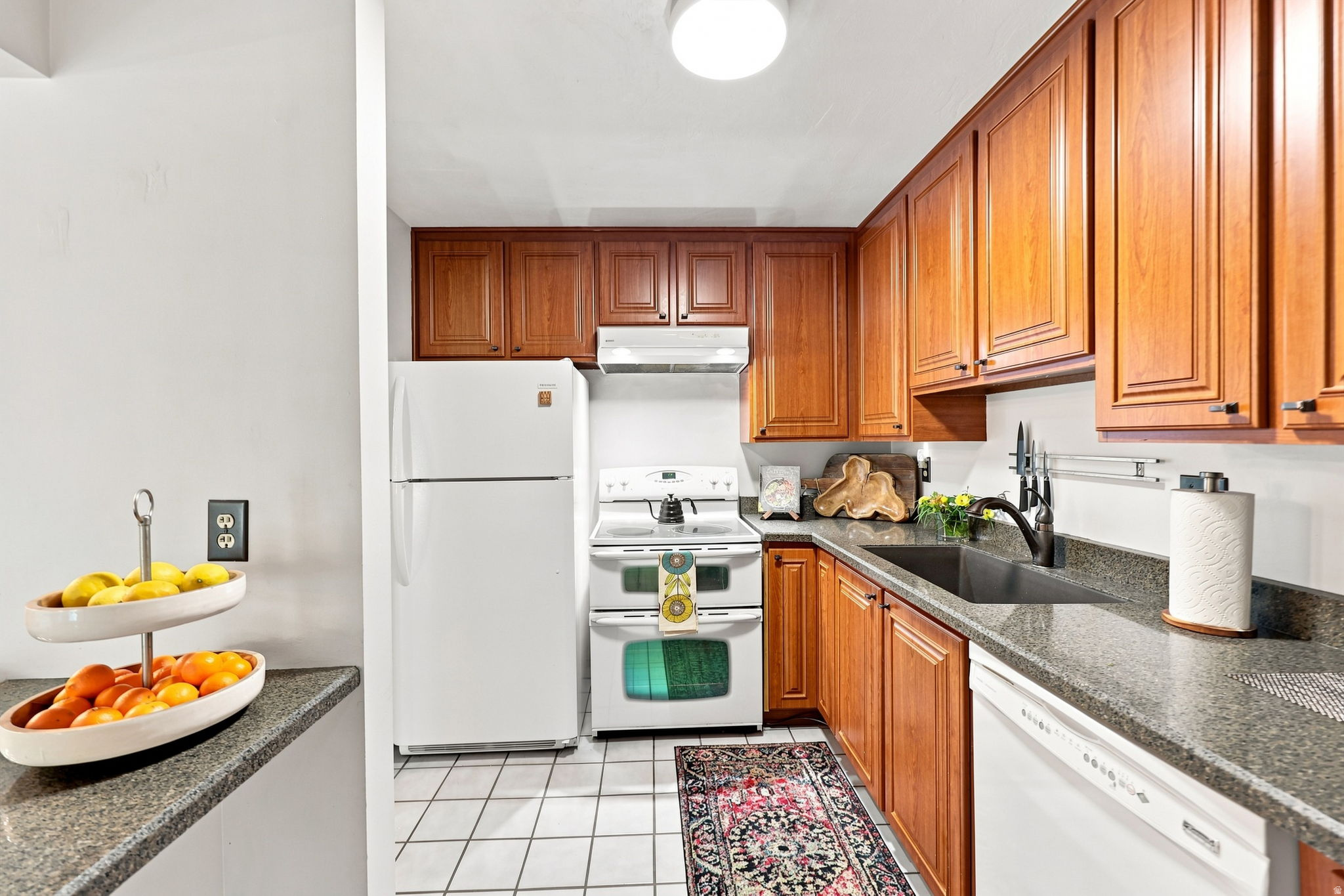 Kitchen featuring wood cabinetry, white appliances, a stainless steel sink, and gray countertops