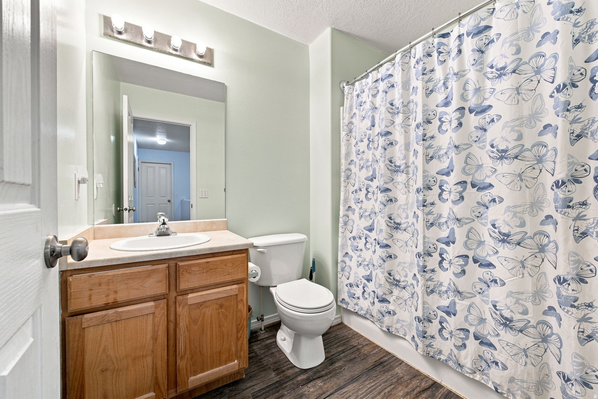 Bathroom featuring a single vanity with wood cabinetry, a large wall-mounted mirror, a shower with a curtain rod, and wood-finish flooring