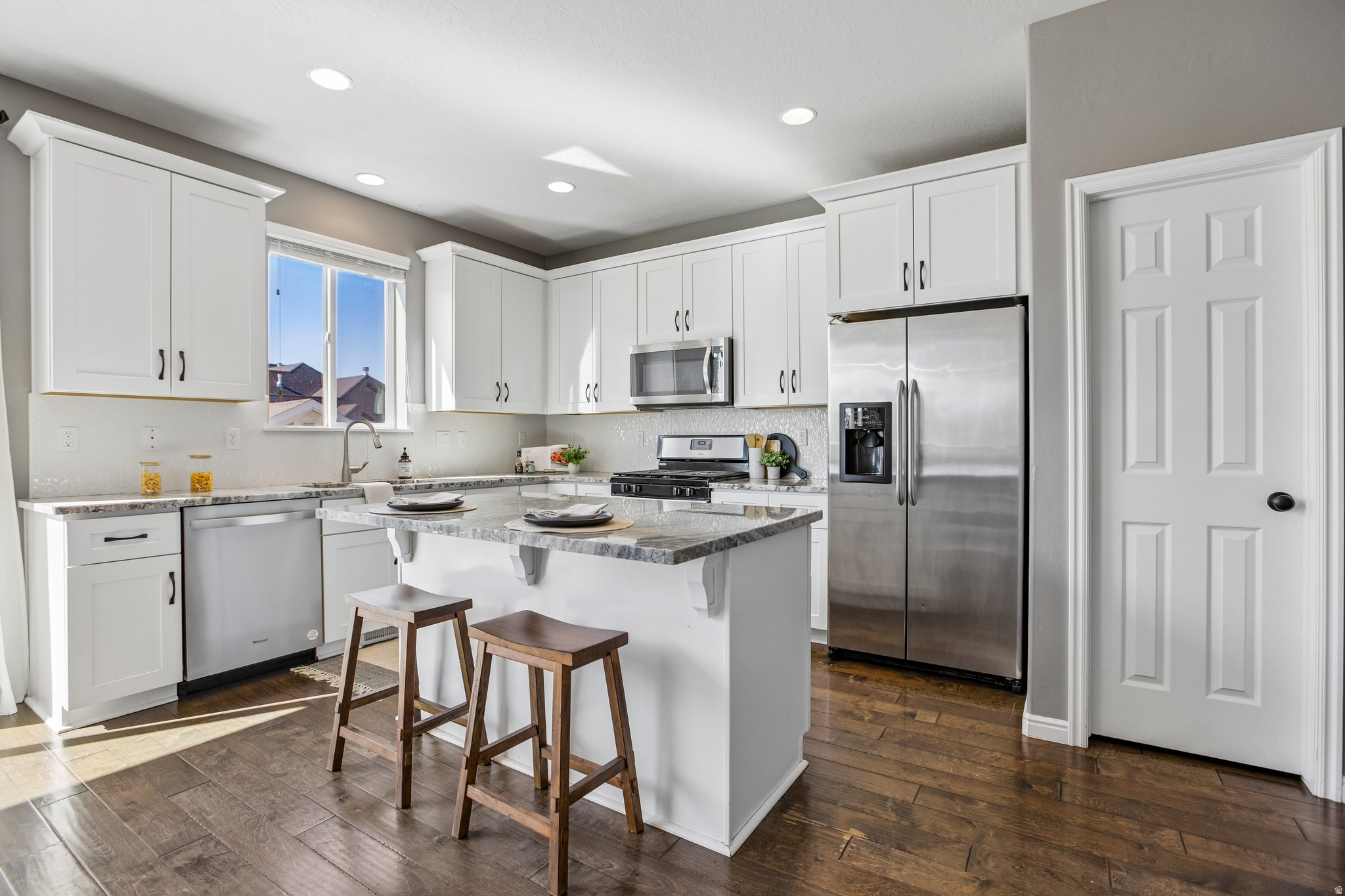 Kitchen featuring white cabinetry, stainless steel appliances, an island with countertop seating, wood-finish flooring, and recessed lighting