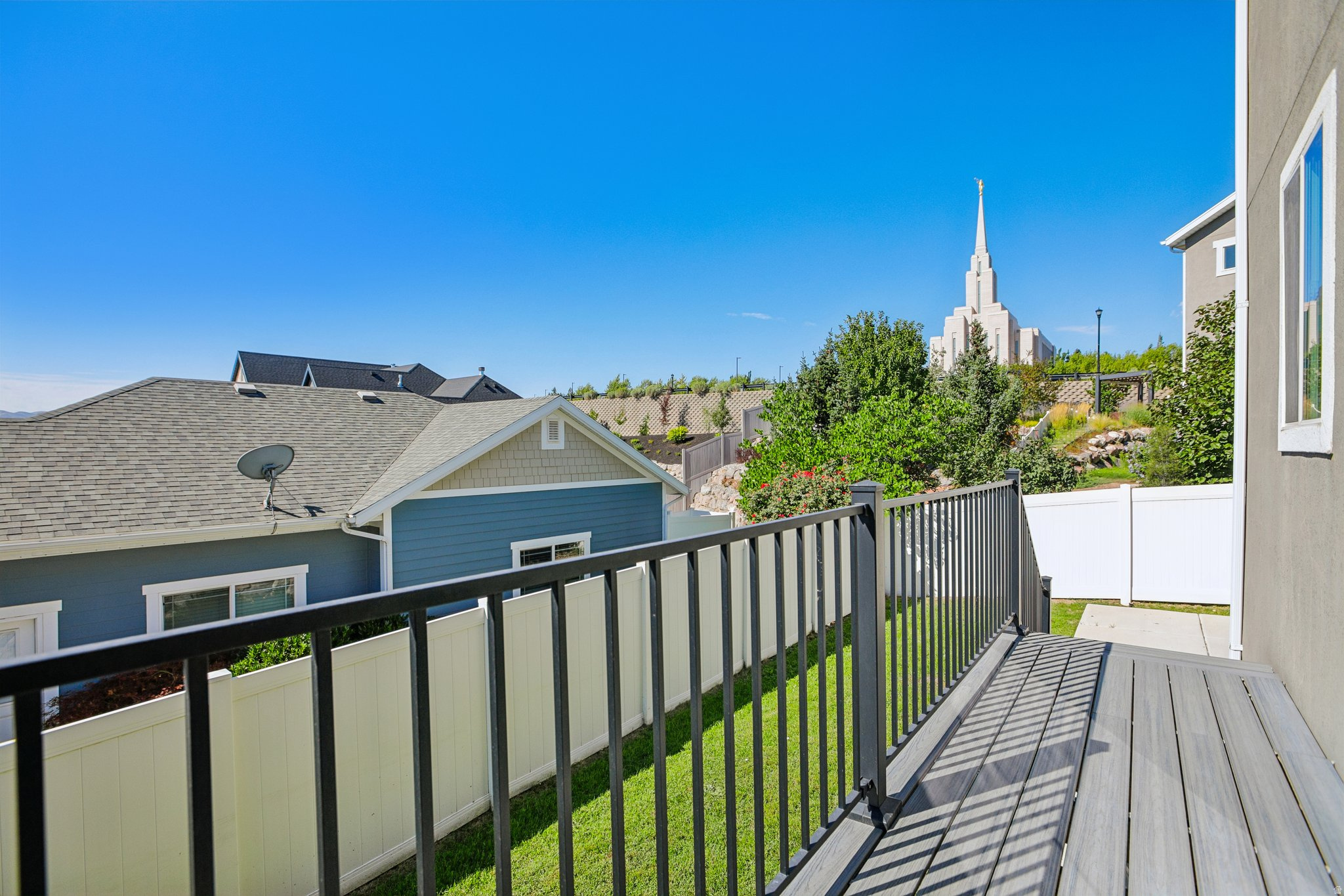 Exterior balcony featuring composite decking, black metal railings, and a white privacy fence
