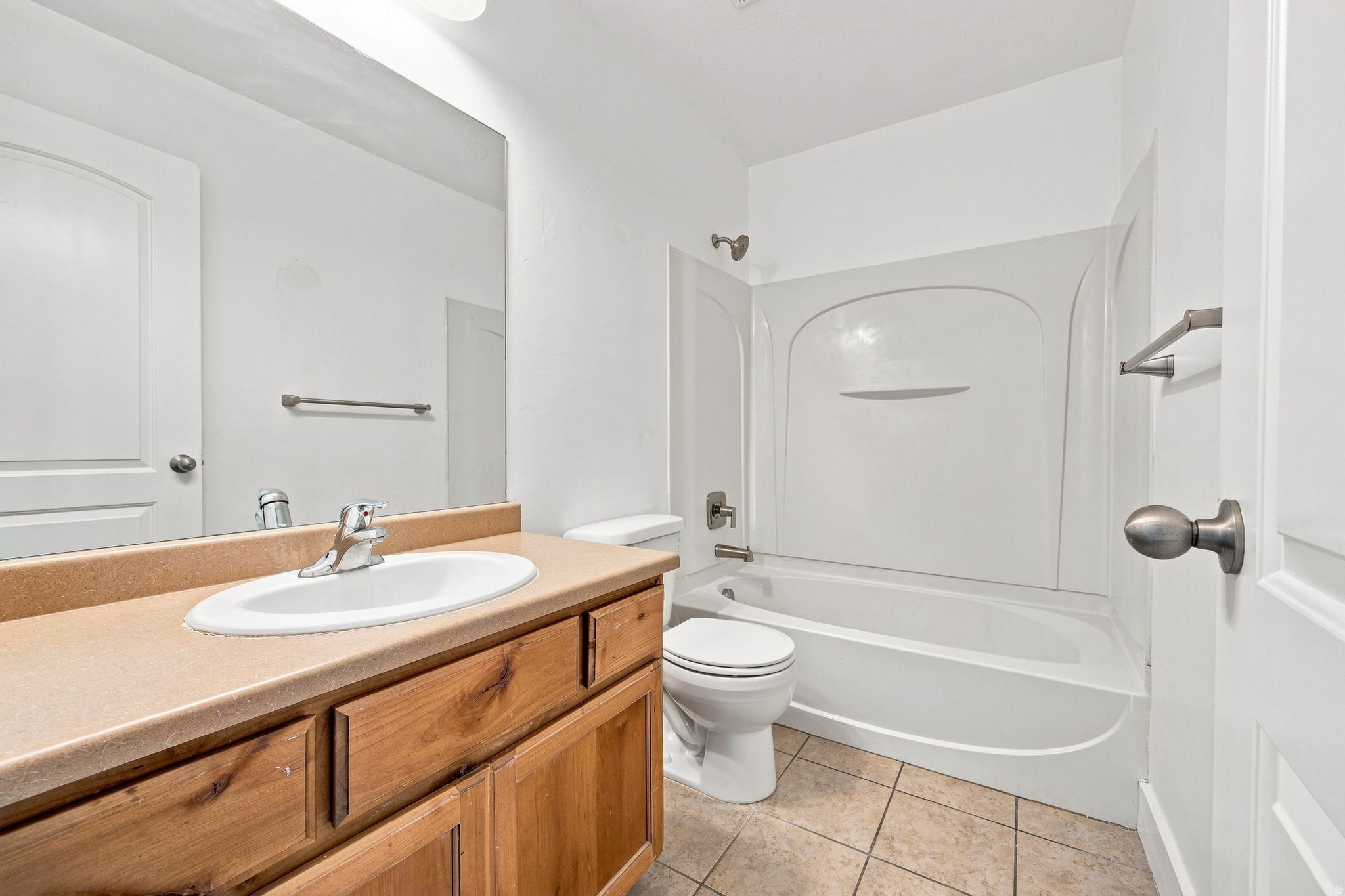 Bathroom featuring a wood-finish vanity with an integrated sink, a full-width mirror, a white bathtub with a shower surround, and tile flooring