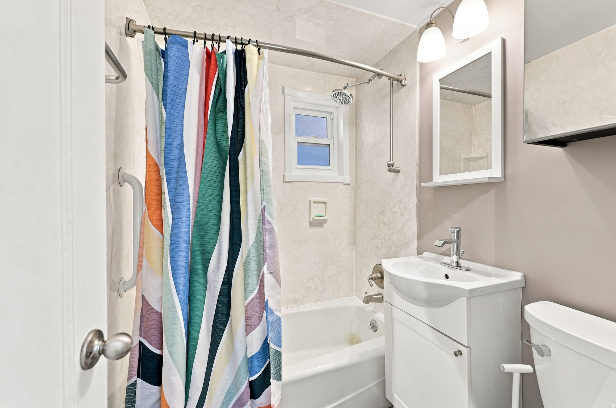 Bathtub with shower fixture, white vanity with integrated sink, wall-mounted mirror, and overhead lighting