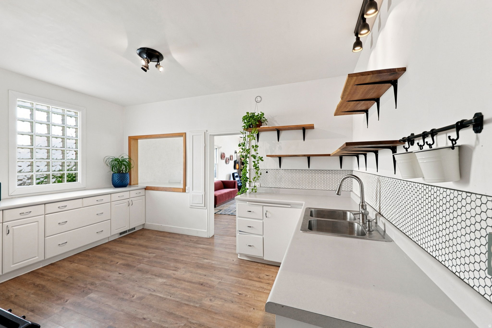 Contemporary kitchen featuring white cabinetry, light countertops, wood-finish flooring, and open wood shelving