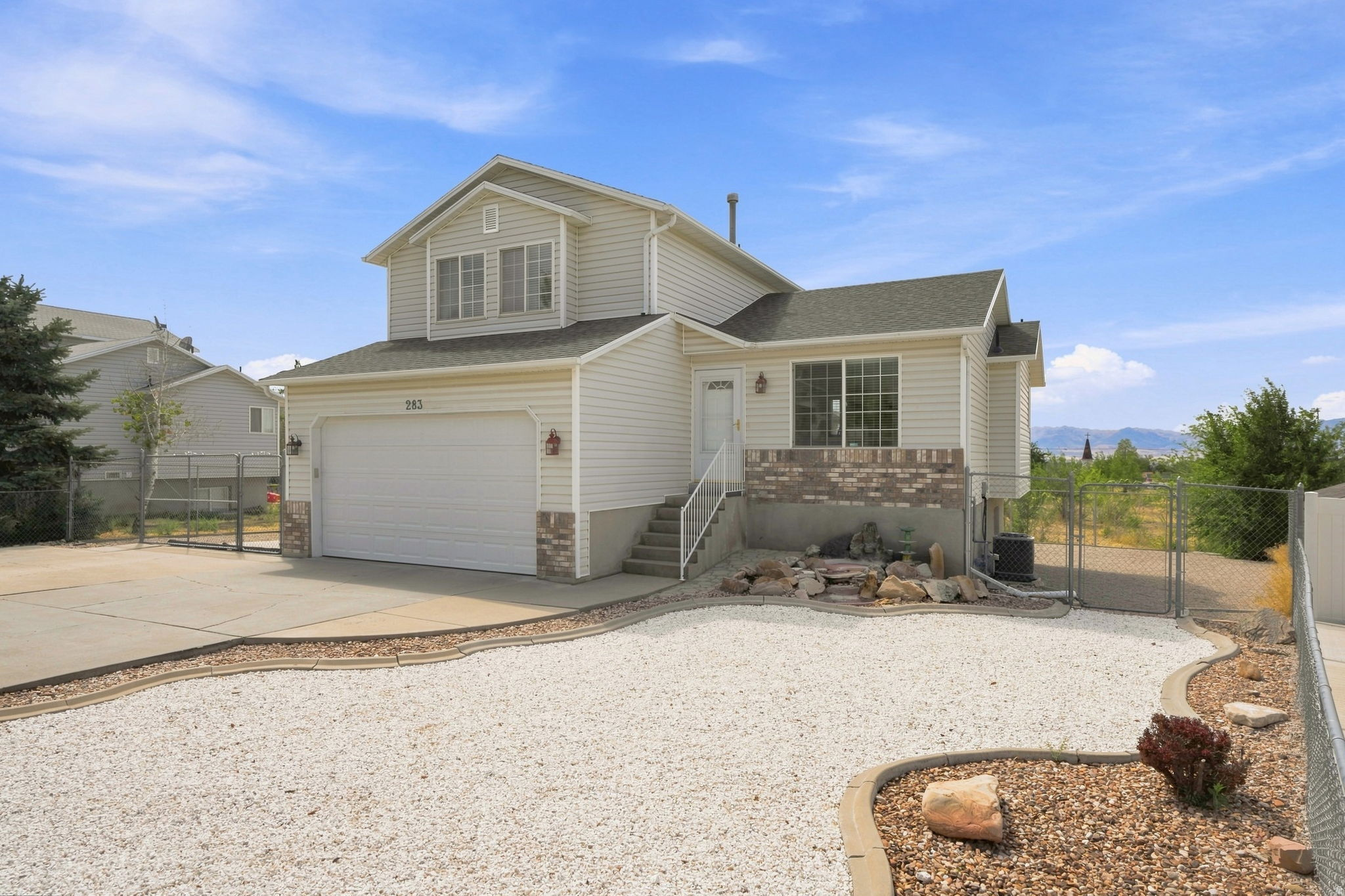 Two-story residence featuring light-colored siding, a two-car garage, and a gravel front yard