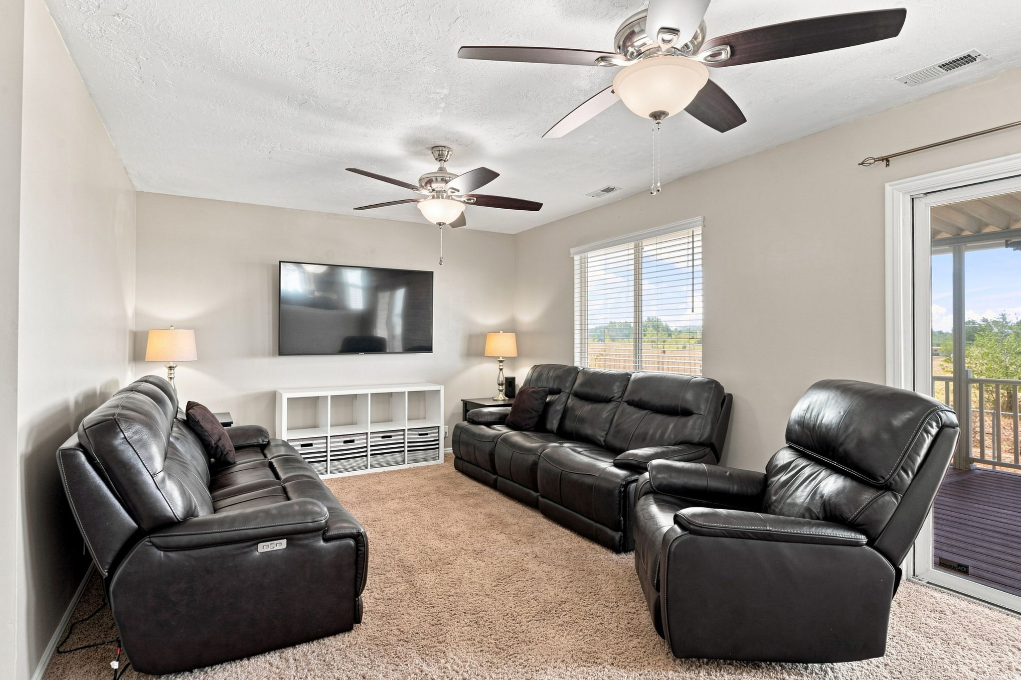 Carpeted living space with multiple ceiling fans, wall-mounted television, and a sliding glass door to an outdoor area