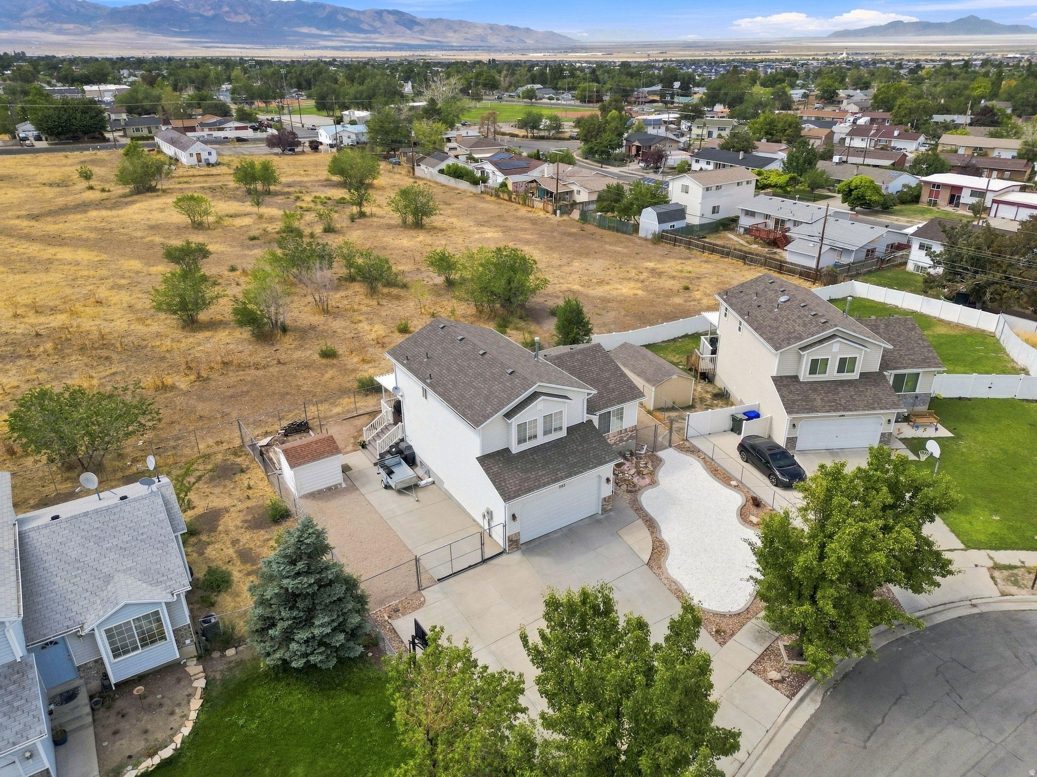 Aerial perspective of a residential property with a light-colored exterior, an attached garage, and a gravel-filled front yard