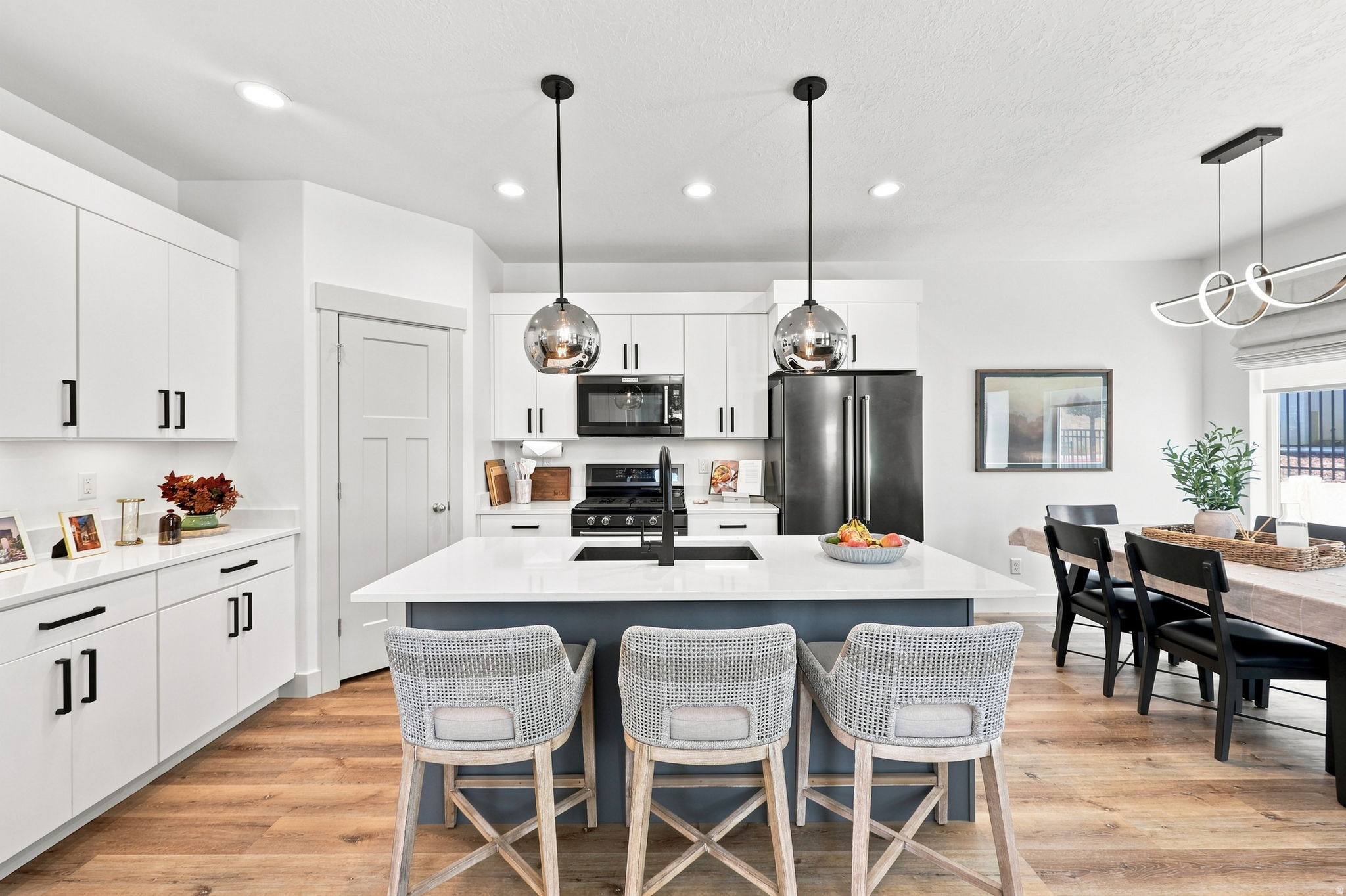 Kitchen featuring white cabinetry, a central island with countertop seating, black appliances, wood-finish flooring, and pendant lighting