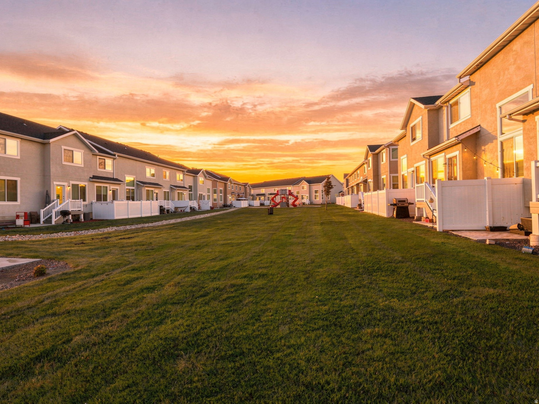 Expansive manicured lawn anchoring a well-planned residential community featuring contemporary single-family homes with covered front porches, multiple stories, and warm exterior lighting