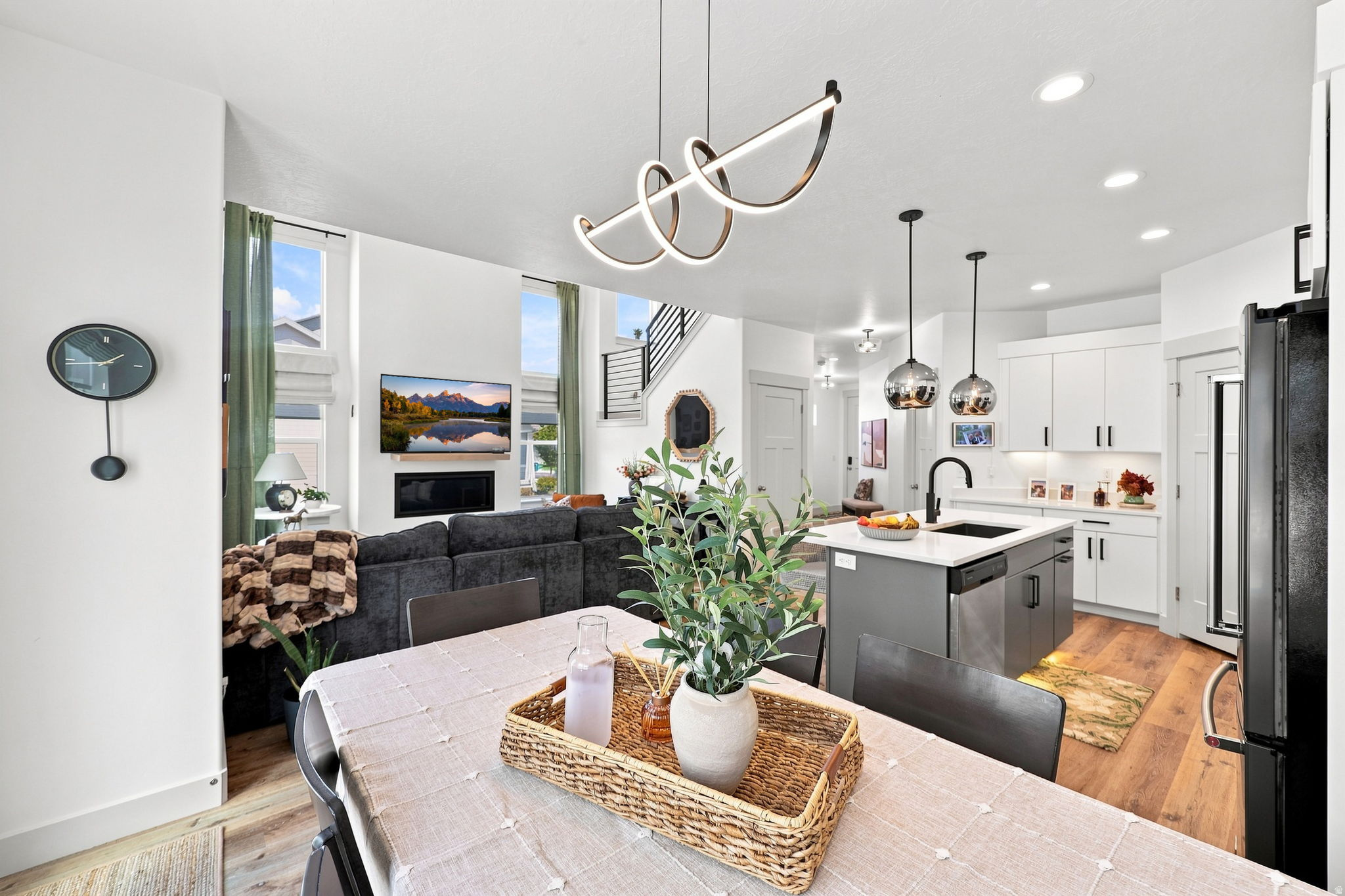 Open-concept living area with high ceilings, wood-finish flooring, a modern kitchen island, and contemporary light fixtures