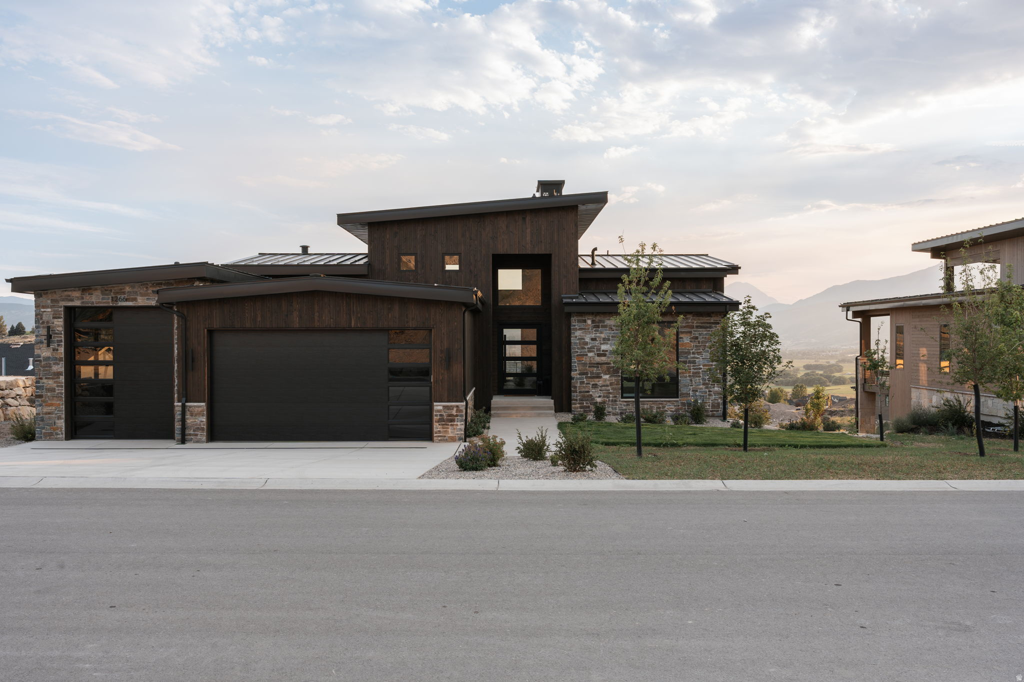 Modern architecture featuring a sloped roofline, wood paneling, stone accents, and integrated garage doors with frosted glass panels