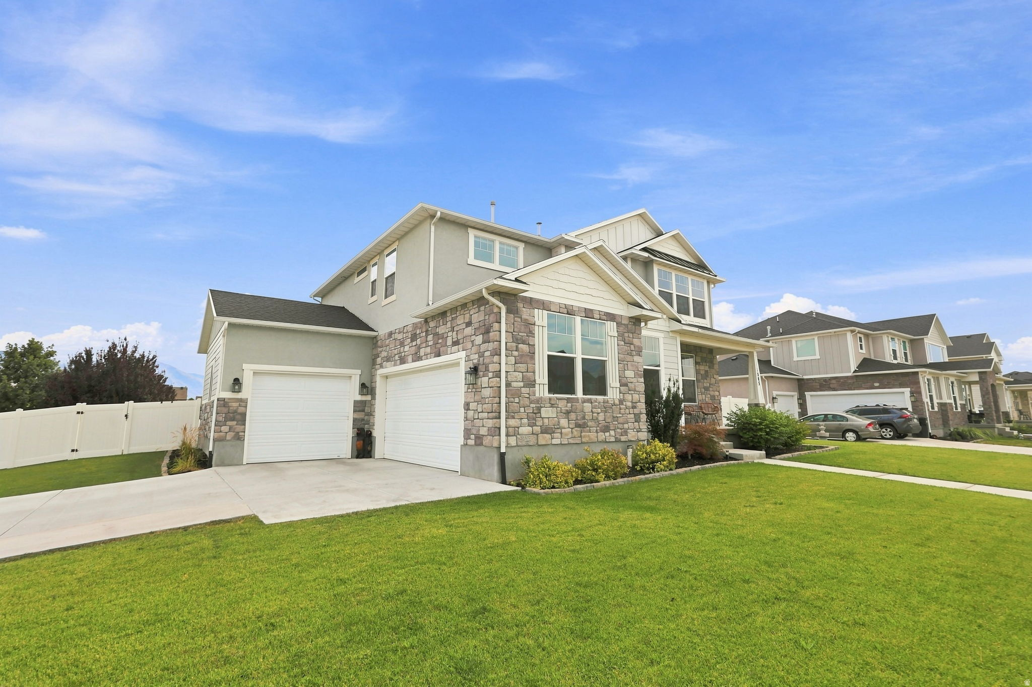 Contemporary residence featuring a two-car garage, stone and siding exterior, a white picket fence, and a concrete driveway