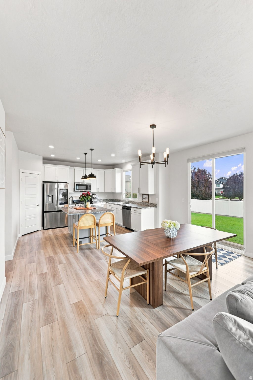 Open-concept living space with wood-finish flooring, a modern kitchen featuring an island with seating, stainless steel appliances, and a sliding glass door to the exterior