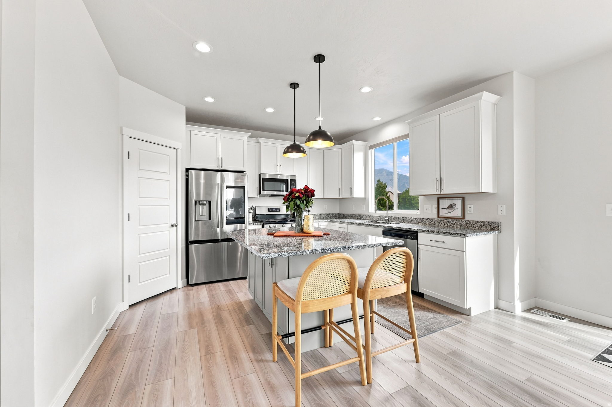 Kitchen featuring a central island with a granite countertop, white cabinetry, stainless steel appliances, and wood-finish flooring