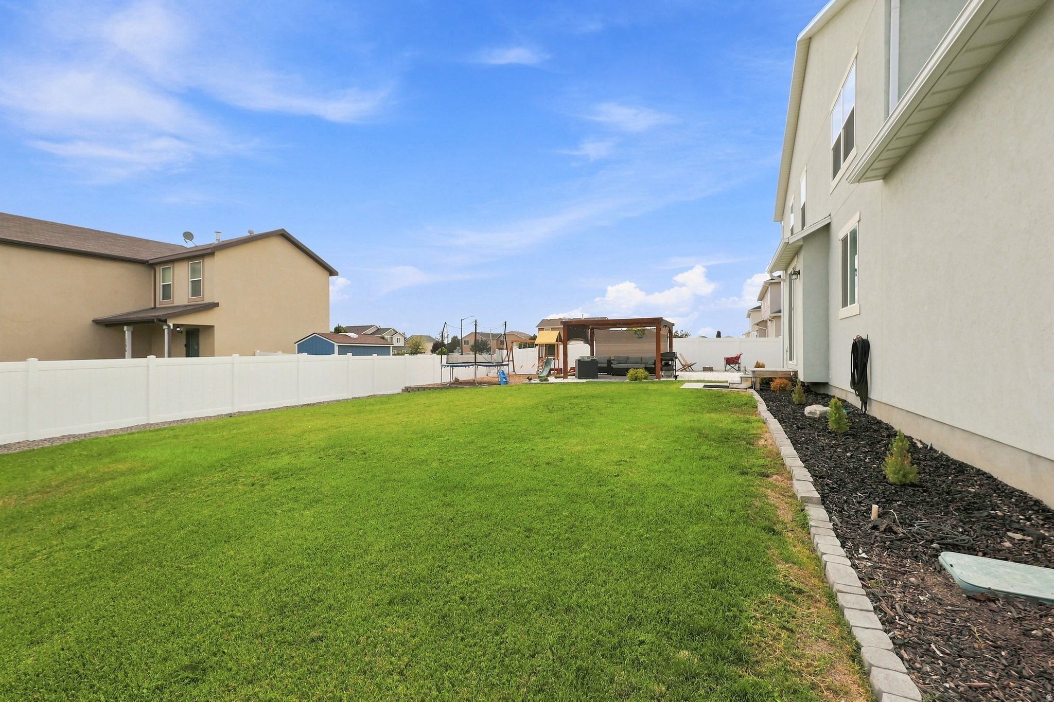 Expansive lawn area with a white privacy fence, mulched planting beds, and a paved patio area