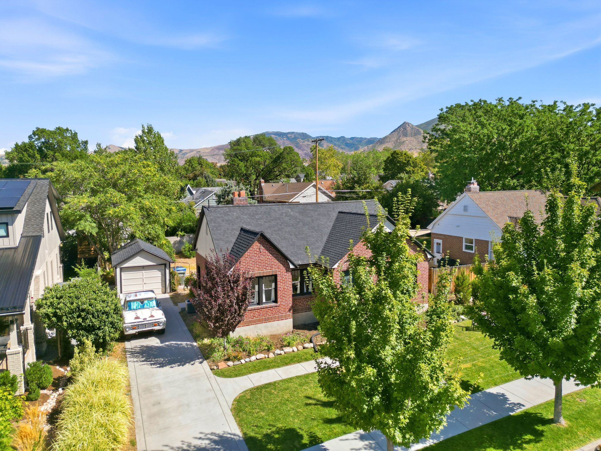 Brick exterior with black roof, attached garage, and landscaped front yard with mature trees