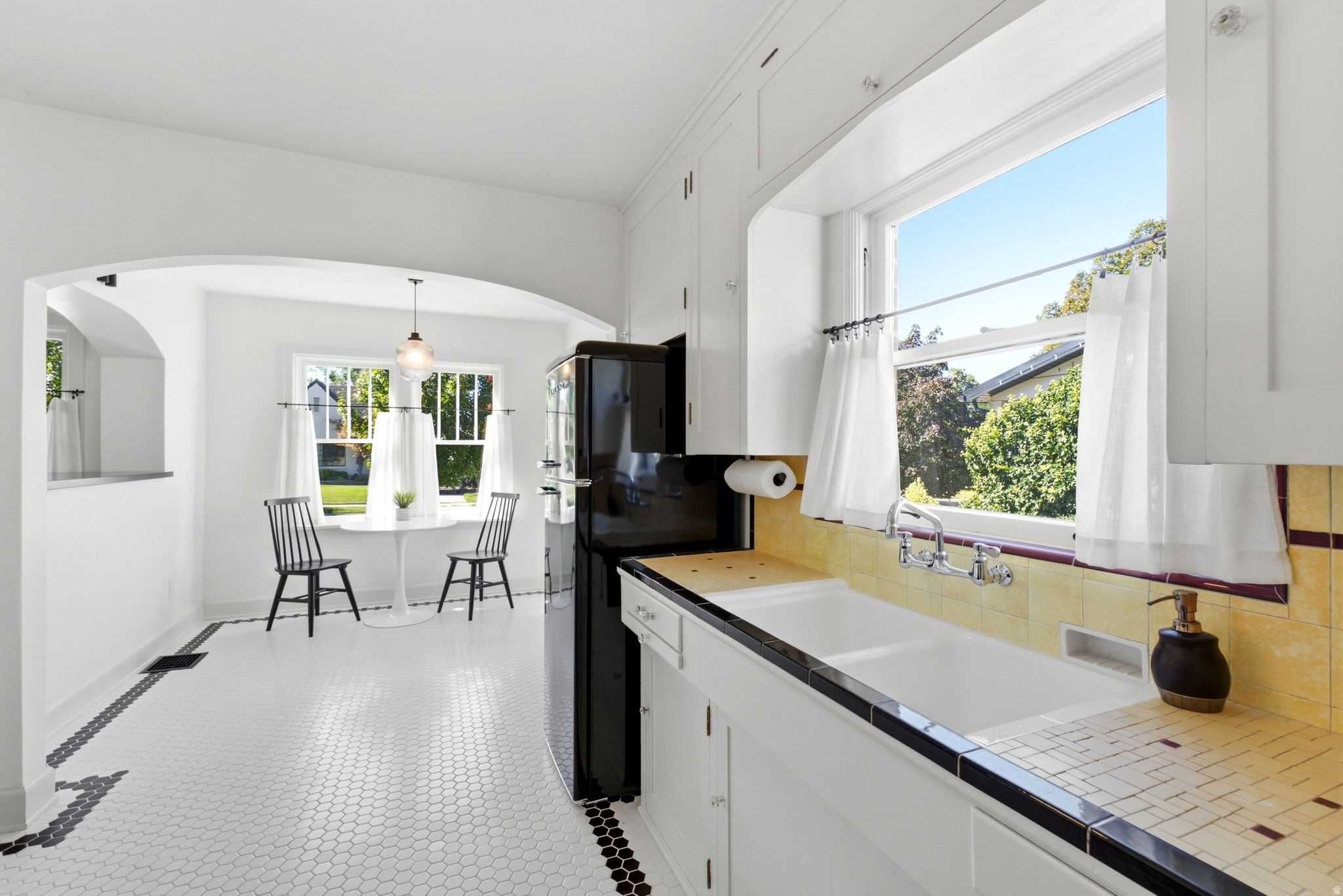 Kitchen with white shaker cabinetry, dual-basin sink, yellow tiled backsplash, and black and white hexagon tile flooring