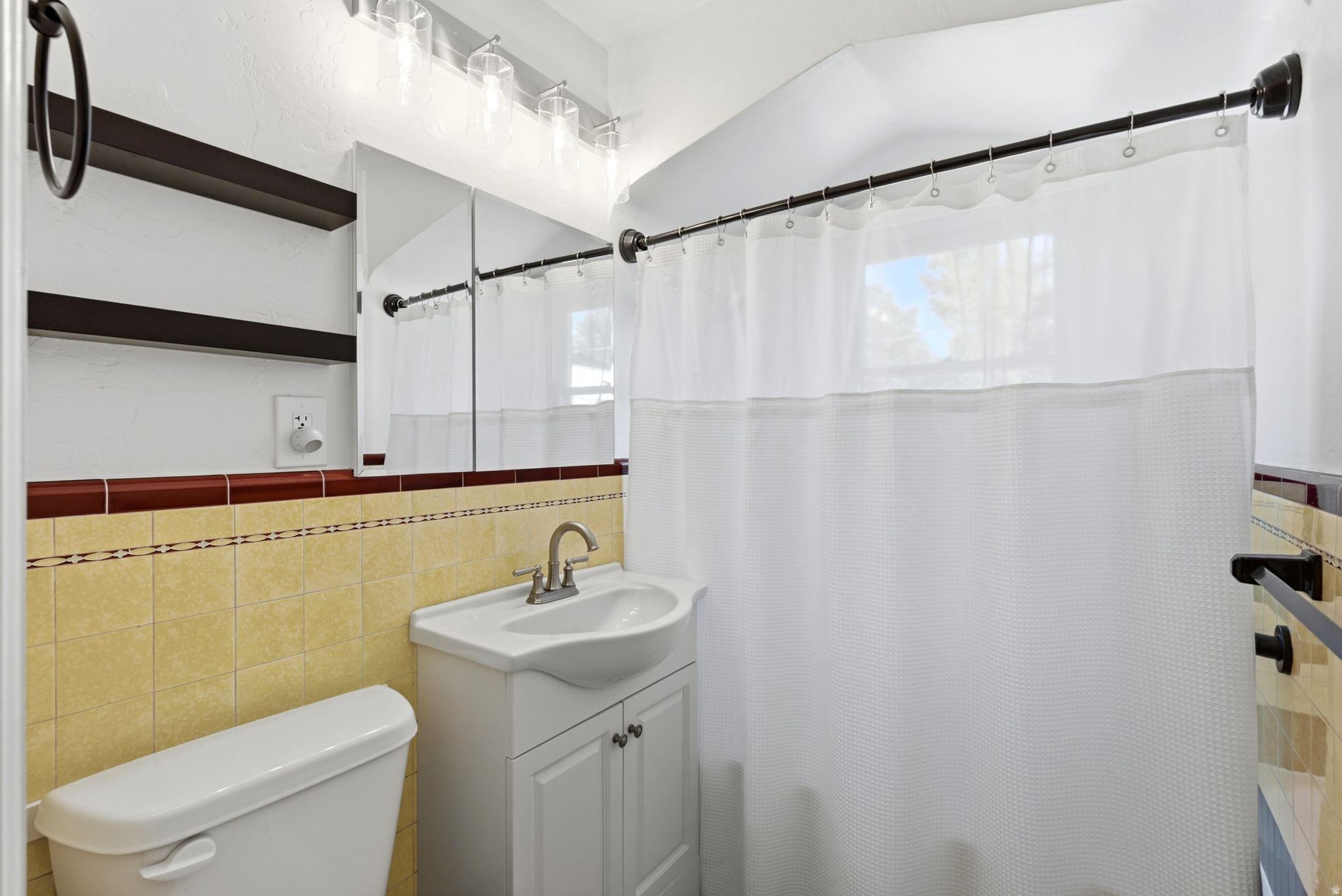 Bathroom featuring a single vanity, wall-mounted medicine cabinet, overhead lighting, and tiled walls with a decorative border