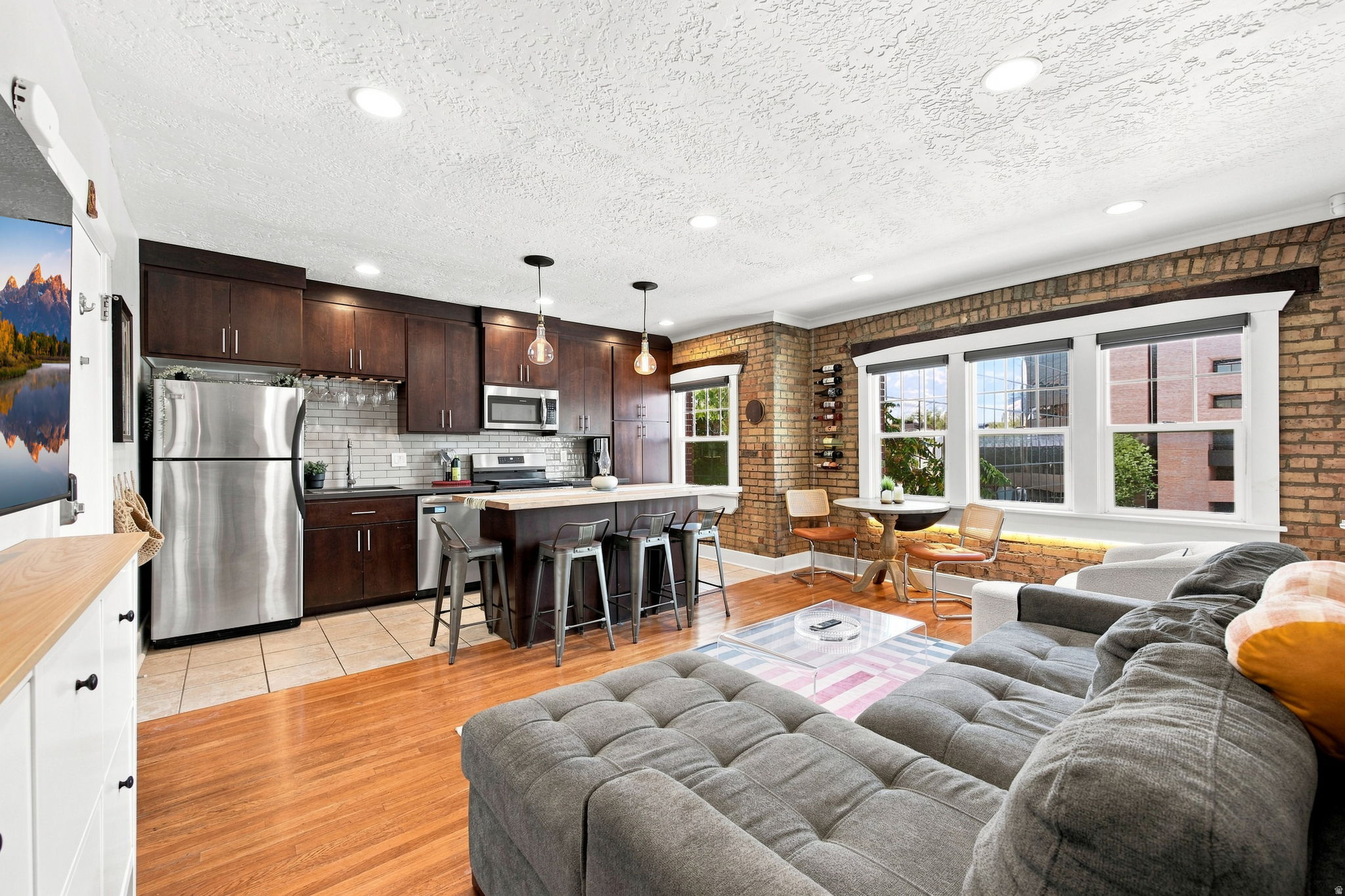 Exposed brick wall, hardwood flooring, stainless steel appliances, dark wood cabinetry, and recessed lighting