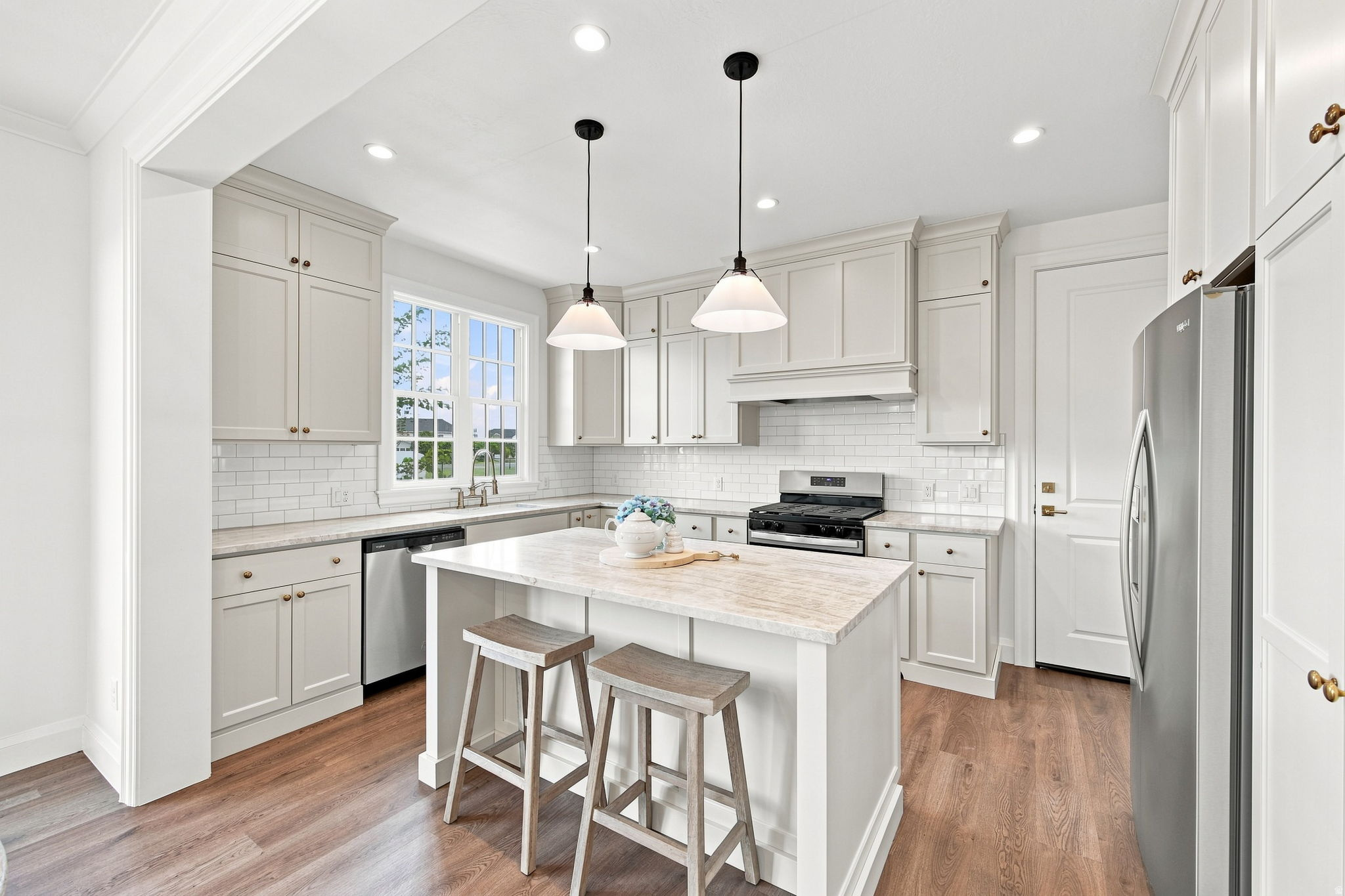 Model Home - Kitchen featuring white cabinetry, subway tile backsplash, an island with countertop seating, stainless steel appliances, and wood-finish flooring