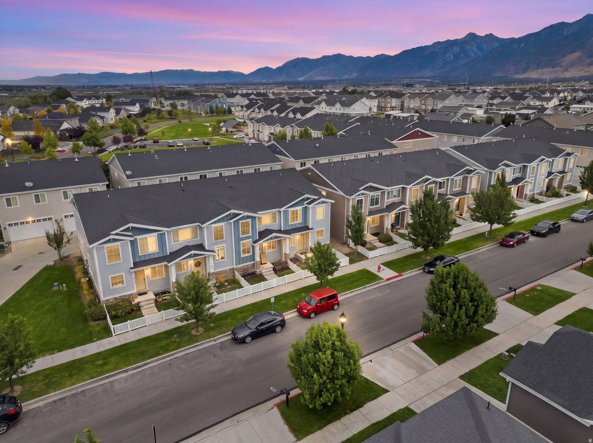 Townhome streetscape featuring varied exterior finishes, landscaped front yards with white fencing, and an expansive mountain range backdrop
