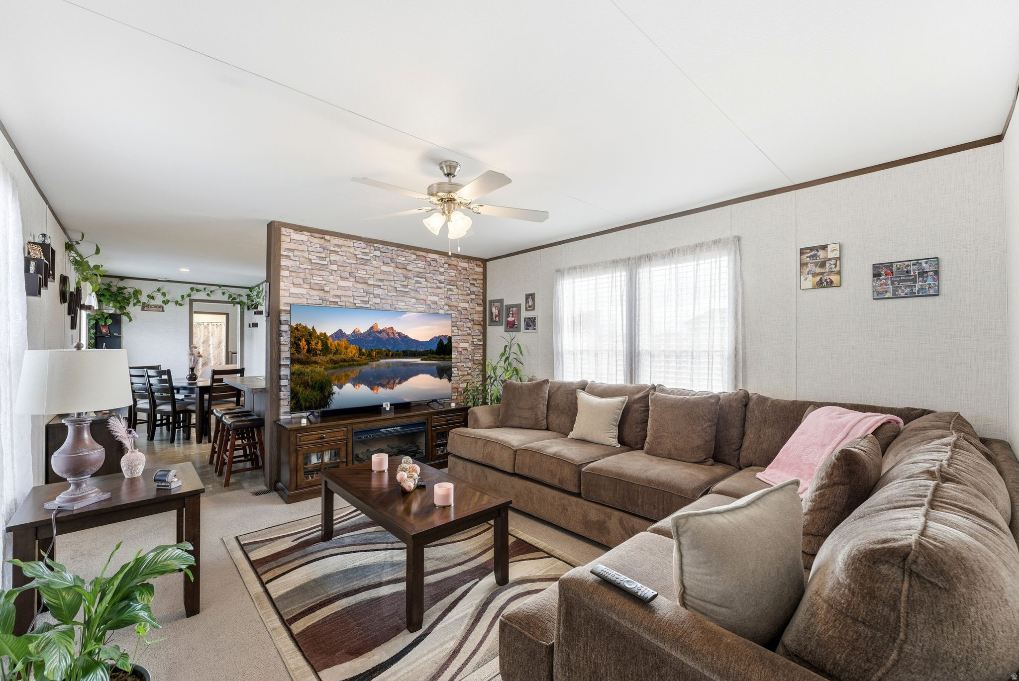 Open-concept living area featuring a stone-accented media wall, ceiling fan, and carpeted flooring