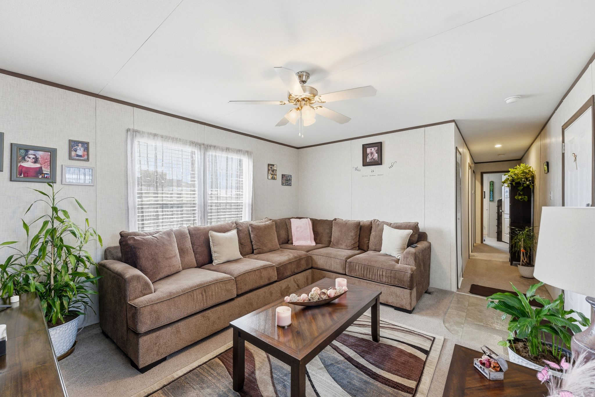 Spacious living area featuring panel walls, a ceiling fan, and multiple windows with blinds
