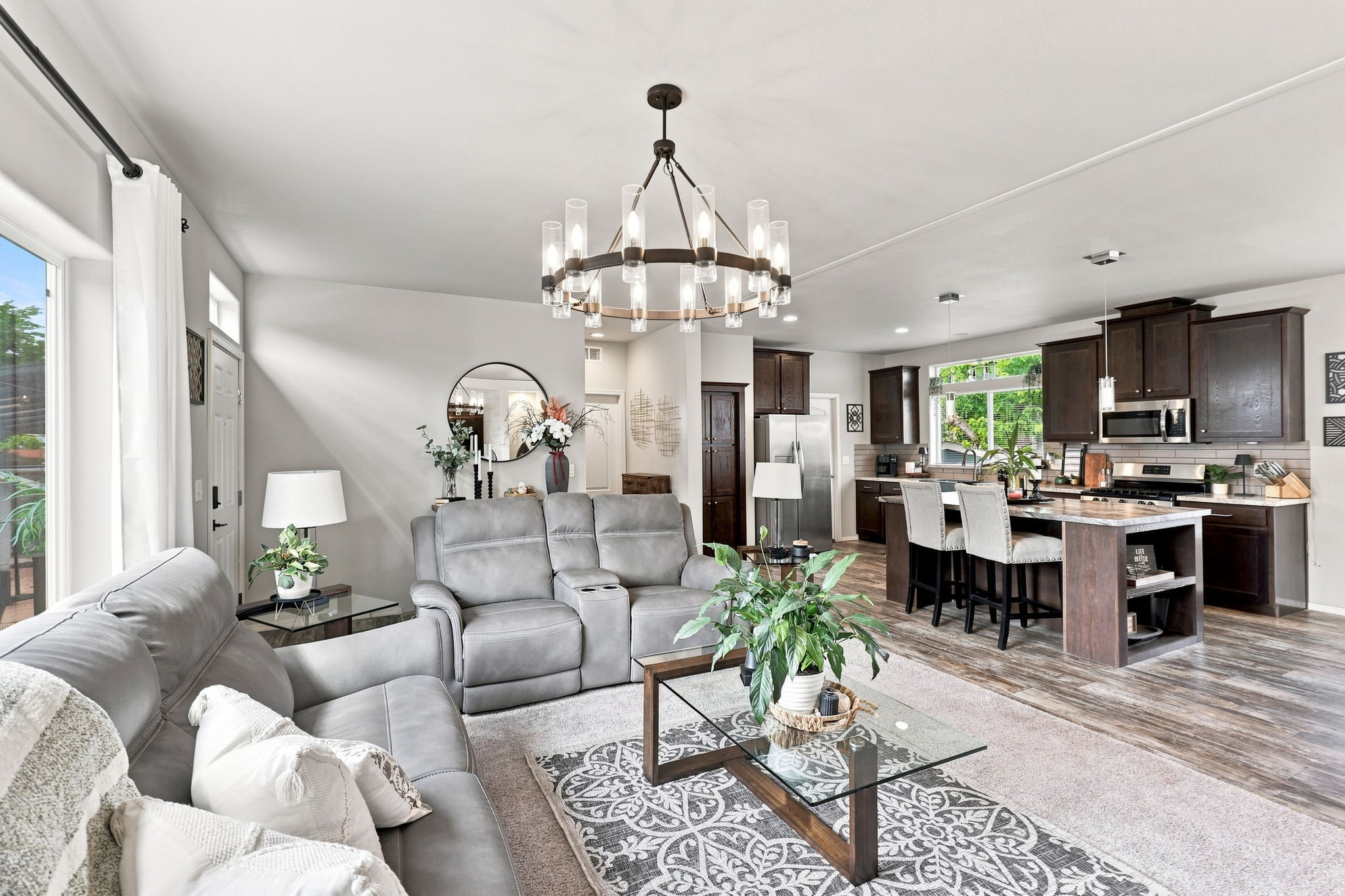 Open-concept living space featuring wood-finish flooring, a contemporary chandelier, dark wood cabinetry, a kitchen island with seating, and a stainless steel appliance suite