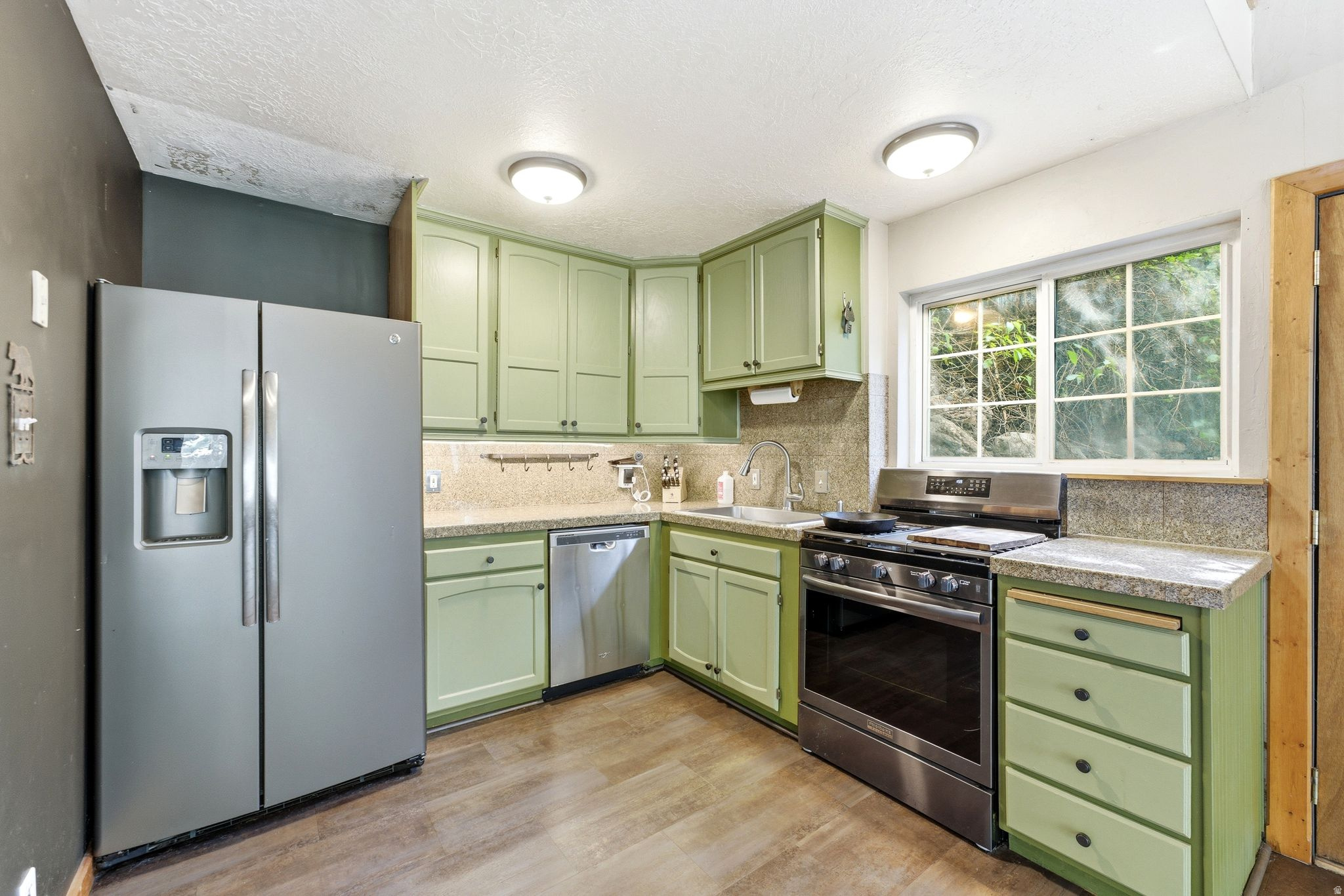 Kitchen featuring wood-finish flooring, green cabinetry, stone-finish countertops, a stainless steel side-by-side refrigerator, and a stainless steel range
