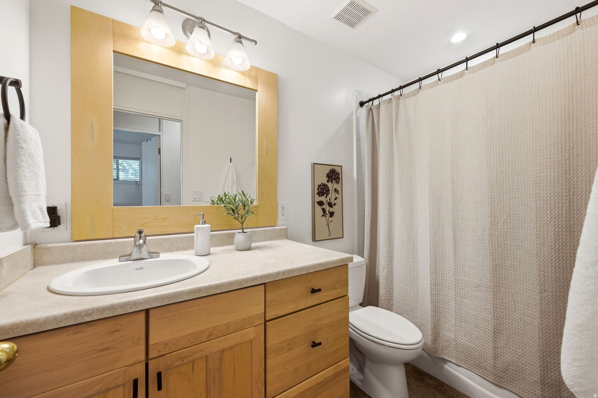 Bathroom featuring a light wood-finish vanity with an integrated sink, a light-toned countertop, and an overhead vanity light fixture