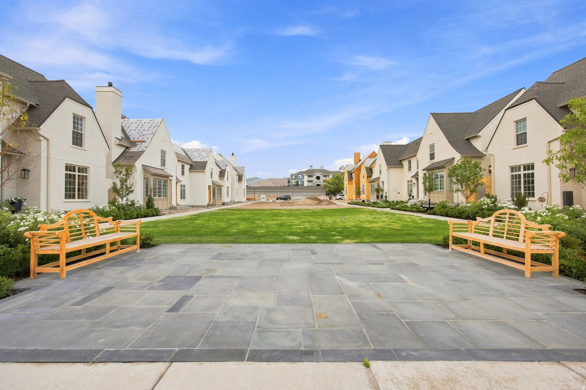 Stone paver patio with a manicured lawn, framed by stucco-clad residences with gabled roofs and multiple windows