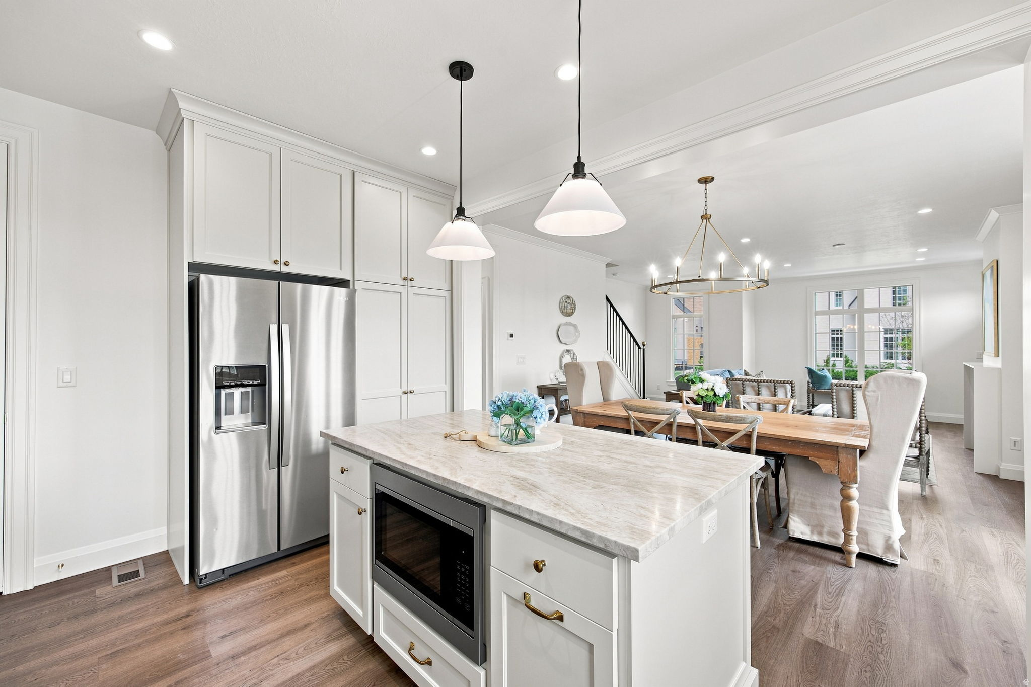 Open-concept living space with wood-finish flooring, white cabinetry, a built-in stainless steel refrigerator, and a kitchen island with stone-finish countertop