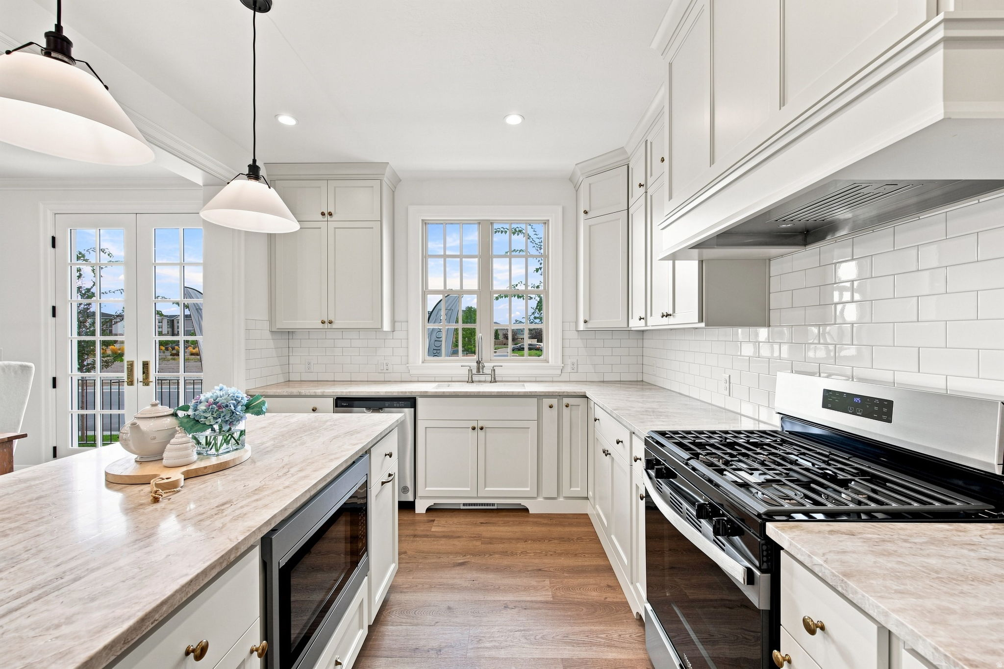 Kitchen featuring a built-in microwave, gas range, wood-finish flooring, white cabinetry, and a subway tile backsplash