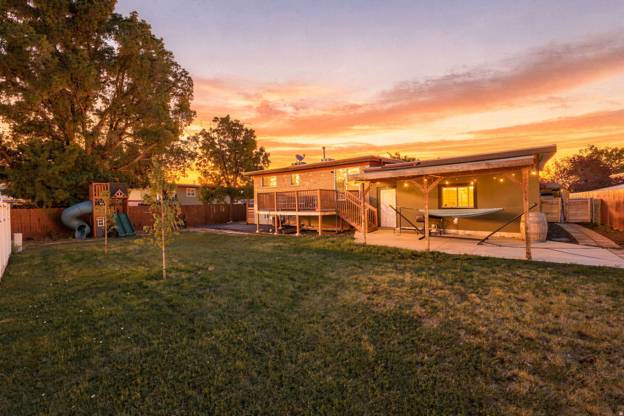 Expansive backyard featuring a lush lawn, privacy fencing, a covered patio with string lighting, and a multi-level wood deck